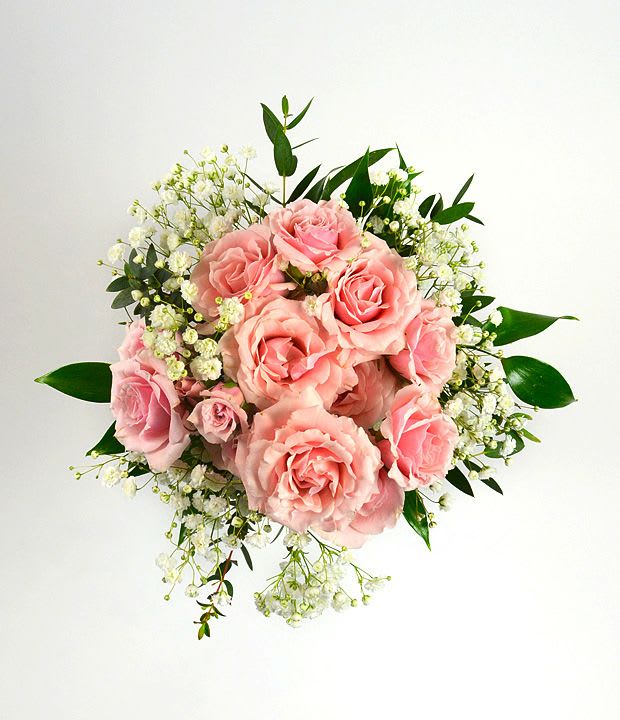 Round bouquet of pink roses and white accent flowers against a white background