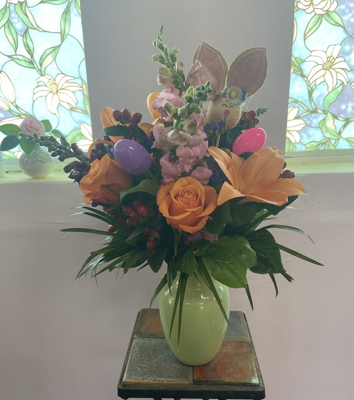 Spring Surprise! - Hop into Spring with this adorable Easter Arrangement! A festive pastel green vase is bursting with Snapdragons, Roses, Asiatic Lilies, Hypericum Berries, and Statice and is adorned with a bunny face pick and easter eggs.