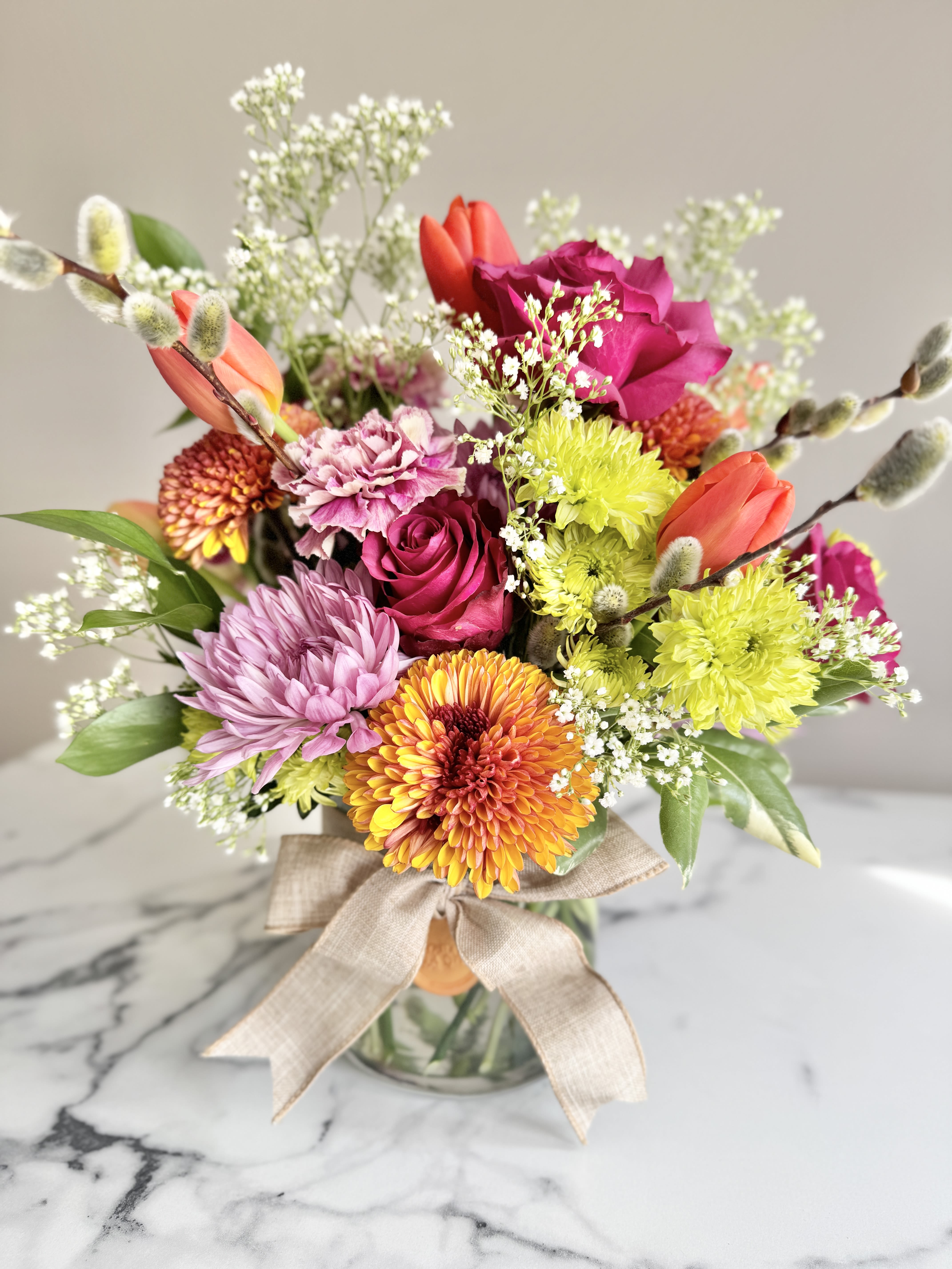 Bright mixed bouquet of roses, tulips, mums, and carnations in a glass vase with a bow