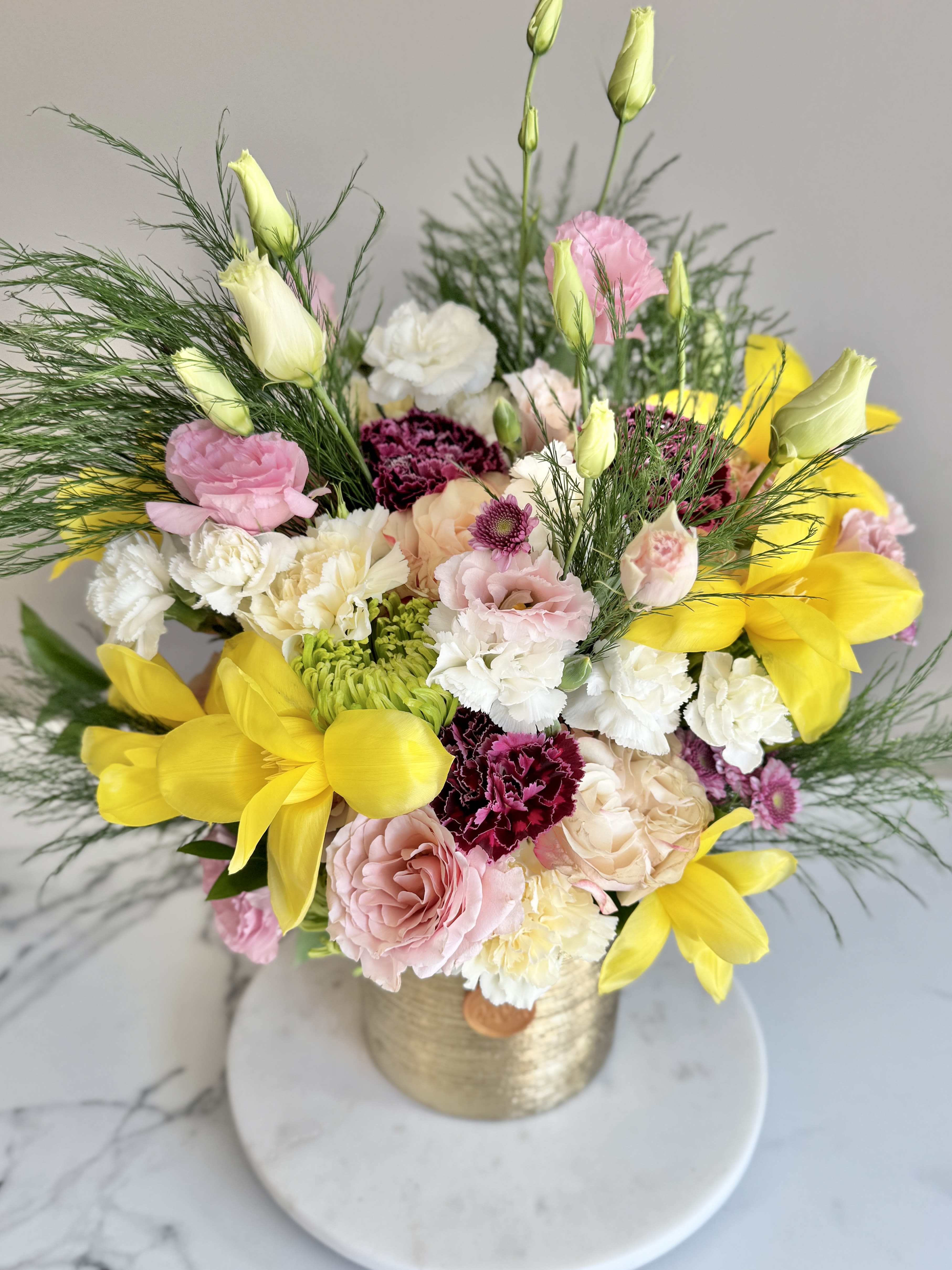 Arrangement of yellow tulips, pink roses, carnations, and white blooms in a gold vase