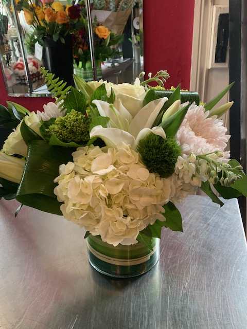 White floral arrangement in a glass vase with green accents