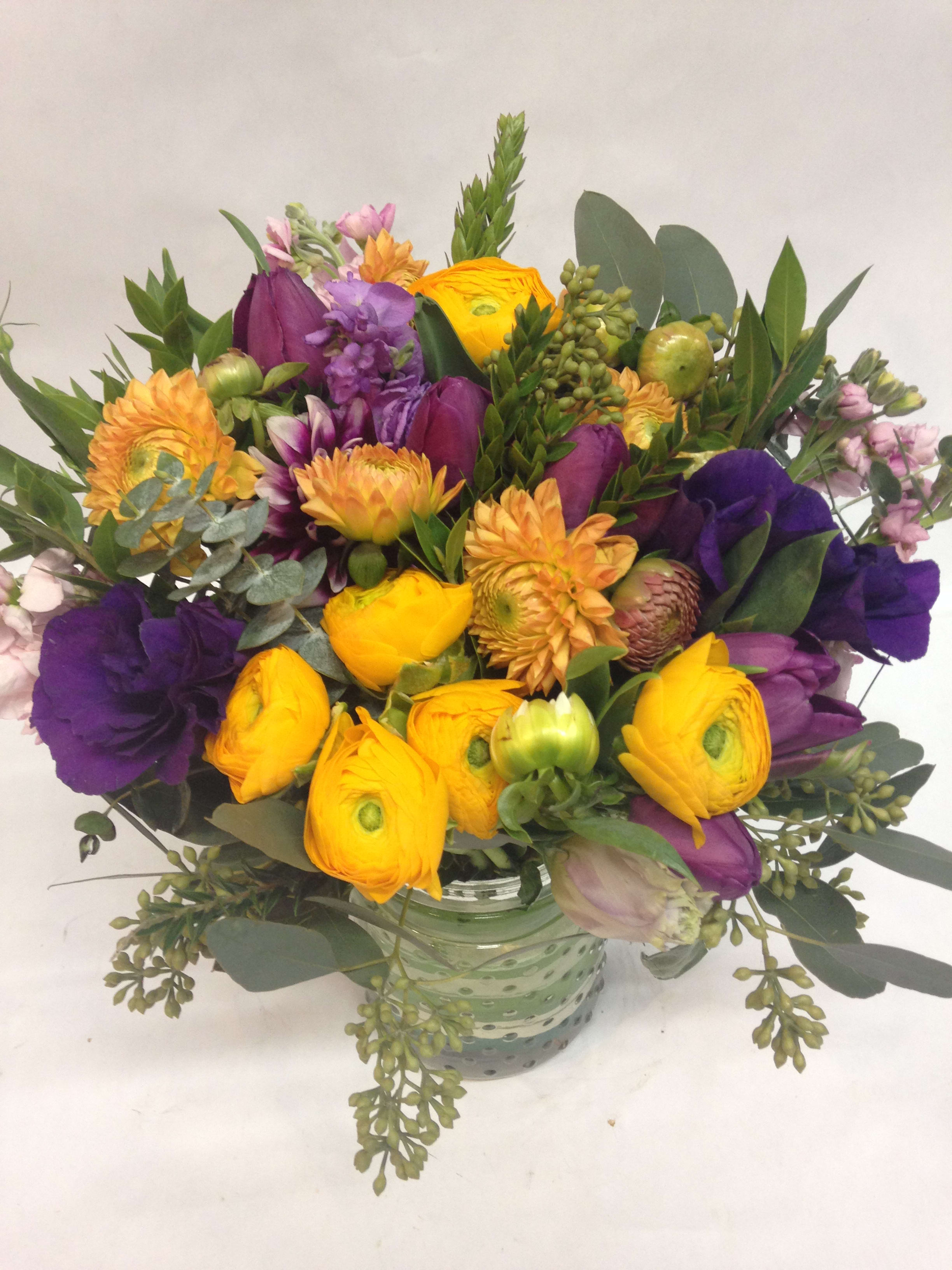 Round arrangement of yellow and purple flowers in a green glass vase