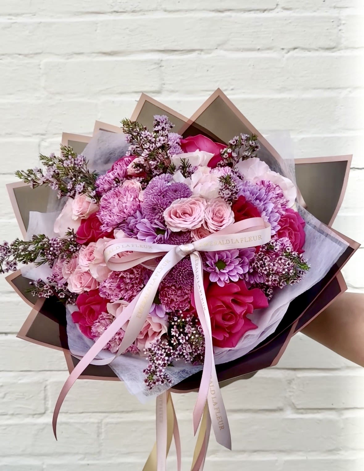 Wrapped in Romance - Designed to be held, presented, and felt. This wrapped bouquet is a study in shape and movement, crafted to create an immediate impression the moment it’s placed in someone’s hands.  Built with a full, rounded silhouette and thoughtfully layered for depth, the composition balances soft, delicate textures with more structured blooms. Each element is intentionally placed to create dimension, allowing the bouquet to feel abundant yet refined from every angle. The signature wrap frames the arrangement with clean, sculptural lines, giving it a polished, gift-ready presence.  Finished with our signature ribbon, a subtle but defining detail that brings everything together. It adds a sense of intention and completion, elevating the bouquet from something beautiful to something truly meaningful.