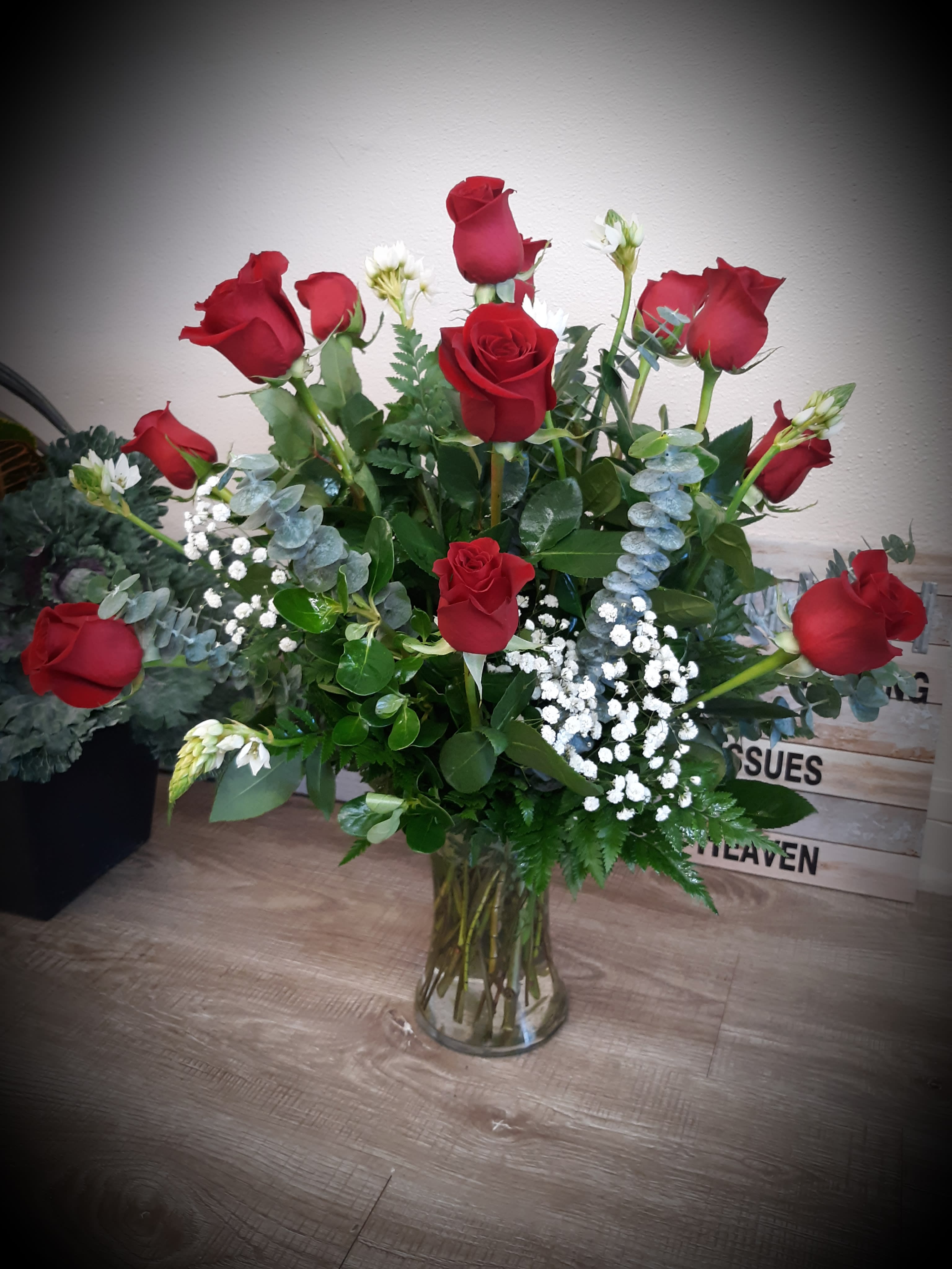 Tall arrangement of red roses with white filler flowers in a clear glass vase