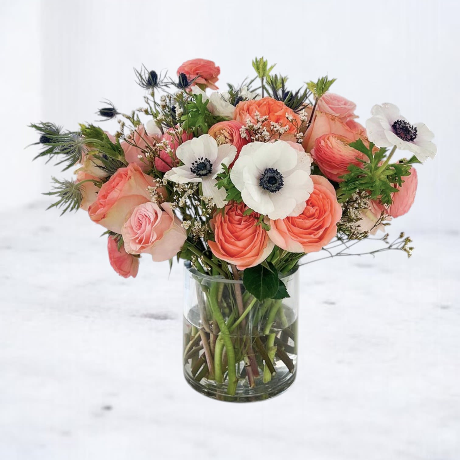 Incarnadine - Incarnadine is a vibrant garden-style arrangement featuring peach roses, coral ranunculus, striking white anemones, and delicate seasonal accents arranged among lush greenery. The warm apricot tones paired with crisp white blooms create a fresh, modern palette full of natural movement and texture.  Designed in a clear glass vase with an airy, organic composition, Incarnadine brings a cheerful yet refined presence to any room. Perfect for thoughtful gestures, celebrations, or sending a bright floral surprise.  Available for same-day flower delivery in Magnolia, Montgomery, The Woodlands, Tomball, Willis, Conroe, and surrounding Houston areas. Flower varieties may vary slightly based on seasonal availability while maintaining the warm peach and apricot palette and natural garden style.  