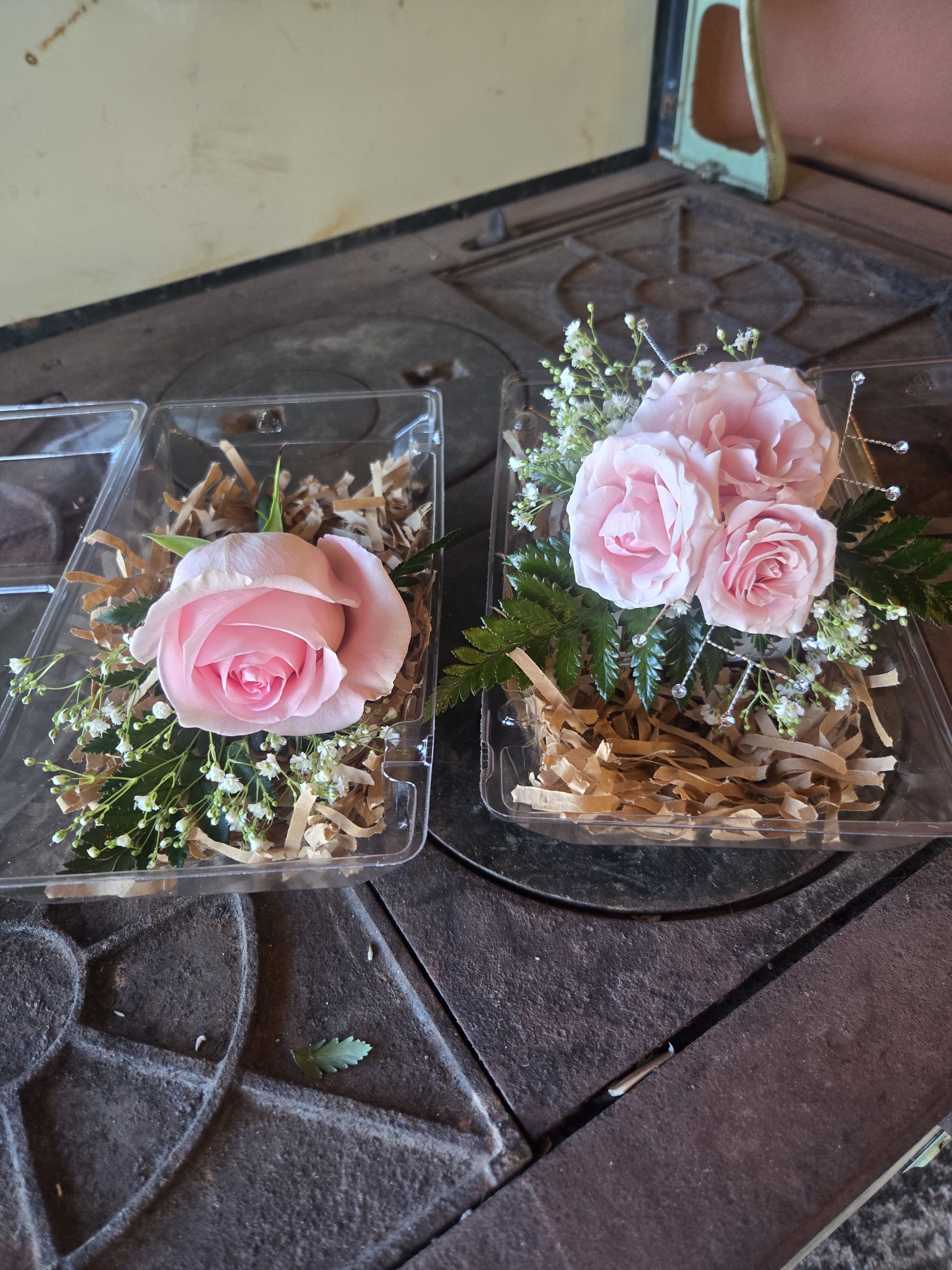 Pink rose corsage and boutonniere set in clear plastic boxes with filler blooms.