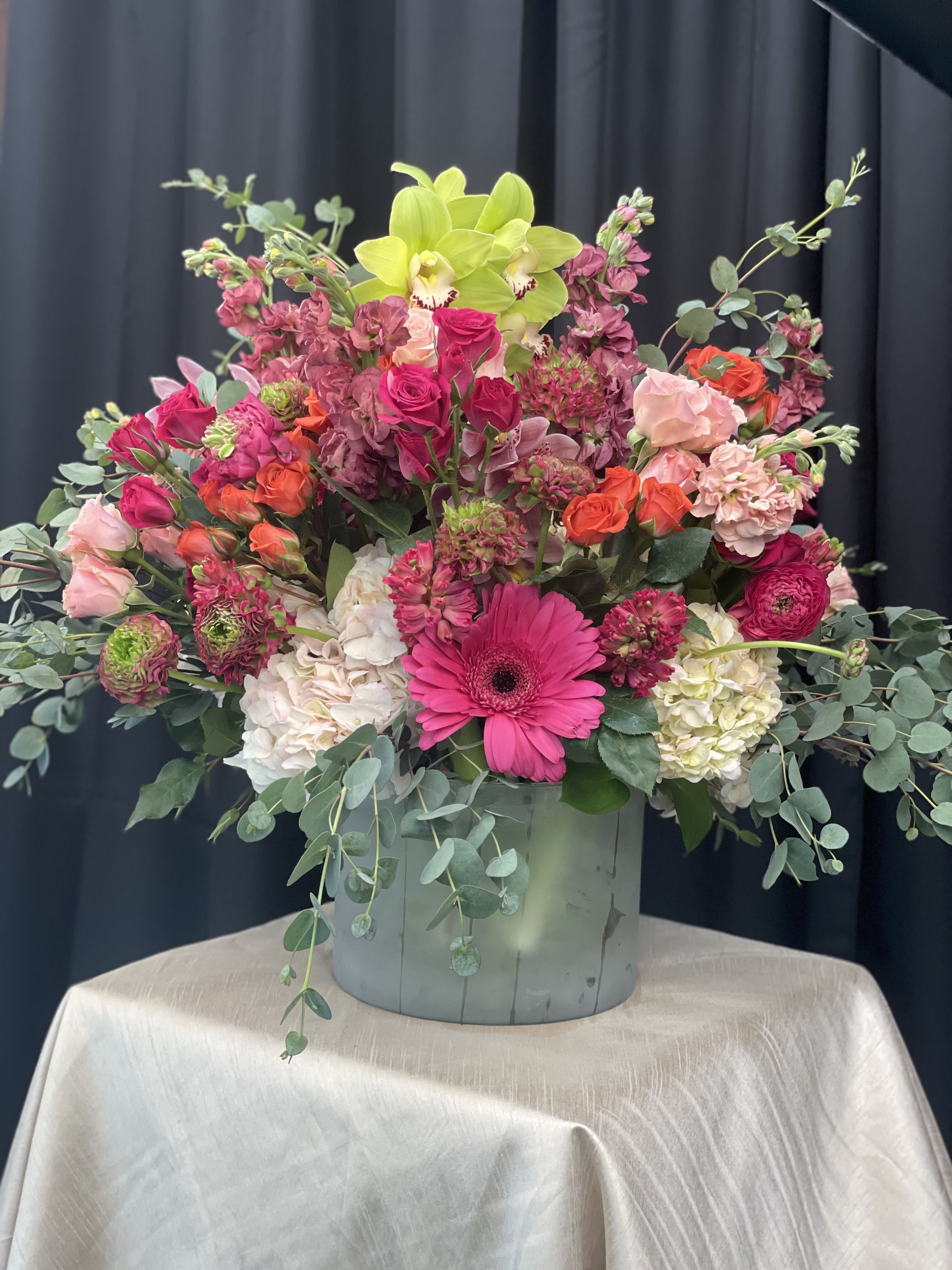 Paradise in Bloom - Paradise in Bloom is a vibrant, high-end arrangement bursting with tropical elegance and bold color. Striking orchids, lush hydrangea, and timeless roses come together in a radiant palette of hot pink, vivid orange, fresh green, and soft light pink. Full of texture and movement, this design feels both luxurious and lively—bringing the energy of an exotic garden into any space.