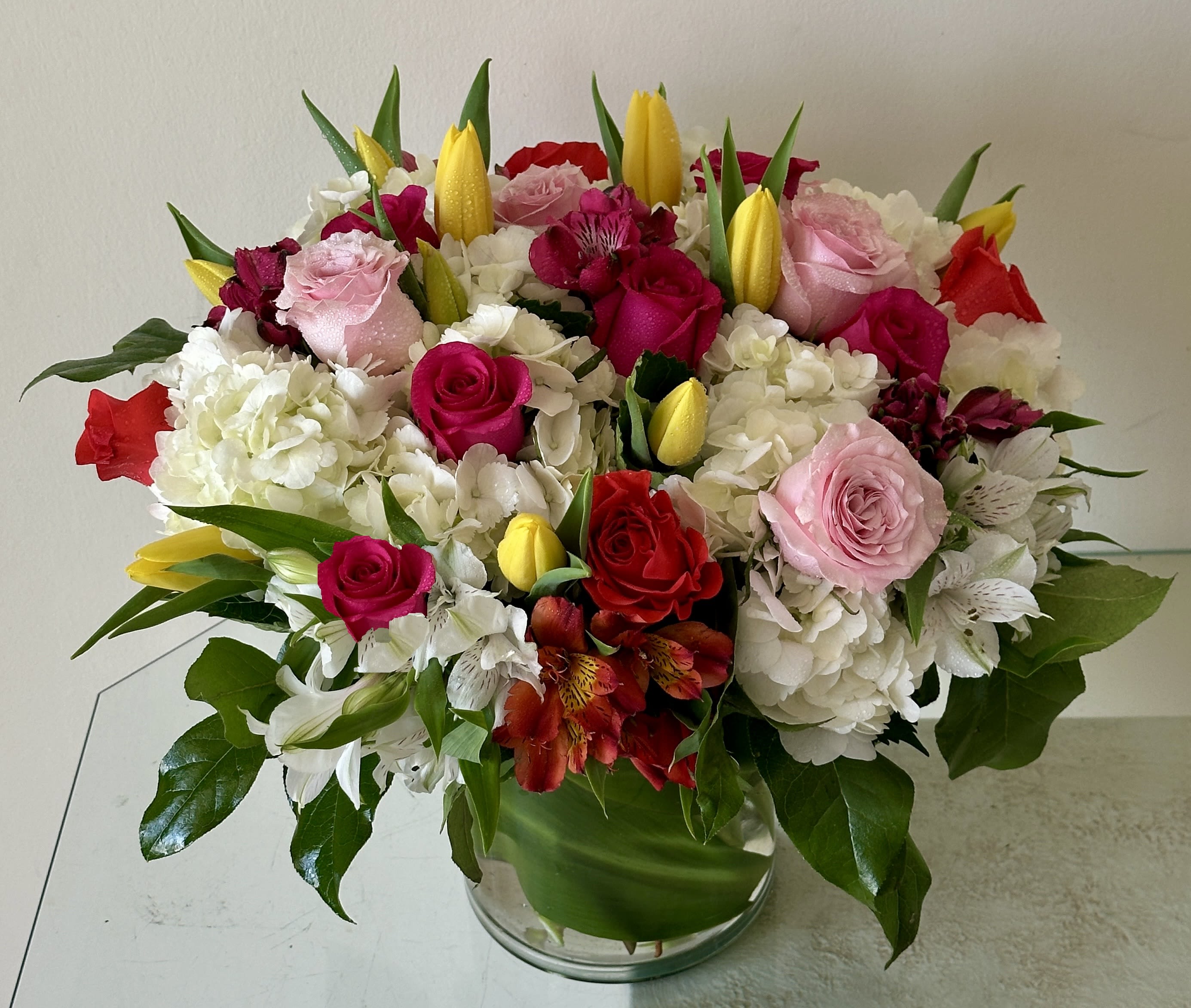 Spring Garden Elegance - An elegant garden-style arrangement featuring premium roses, lush hydrangeas, and fresh tulips in a clear vase with a modern leaf wrap.