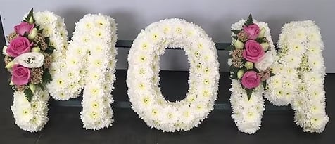 "MOM" or "DAD" Floral Tribute Spray - A beautiful and meaningful tribute, this custom sympathy arrangement is designed in the shape of the word “MOM” or “DAD.” Please note that you must choose one when ordering. The price is for one piece.  Each piece is carefully crafted using white cushion daisies, creating a clean and elegant display that honors your loved one with simplicity and grace.  The words measure approximately 12 inches in height and 36 inches in length, and are accented with a delicate floral accent on the end letters for a soft touch of color.  This is a custom design that requires a few days’ notice. Please call the shop to place your order and allow us to create something truly special for your tribute.