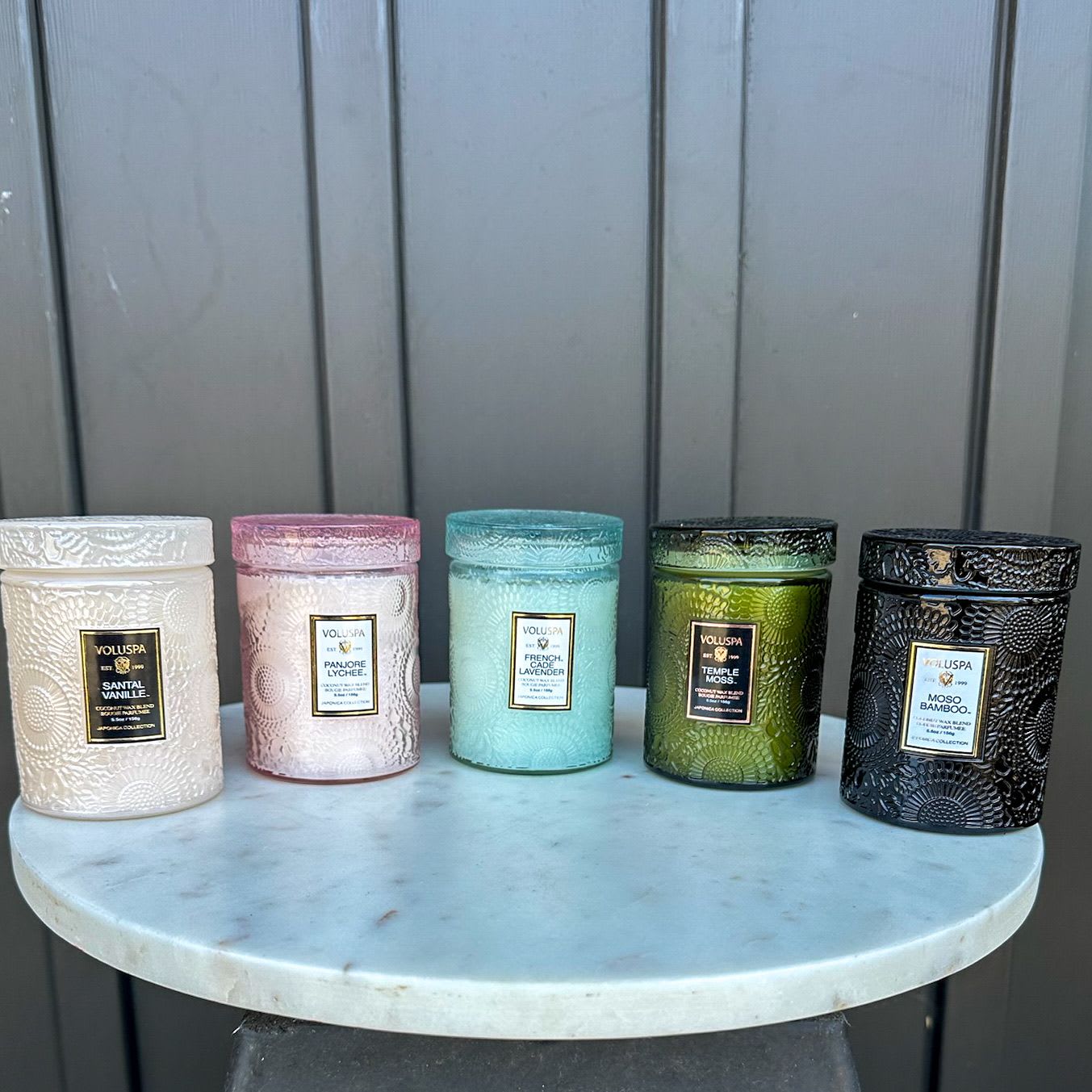 Set of five embossed glass jar candles in assorted colors on a round marble stand.