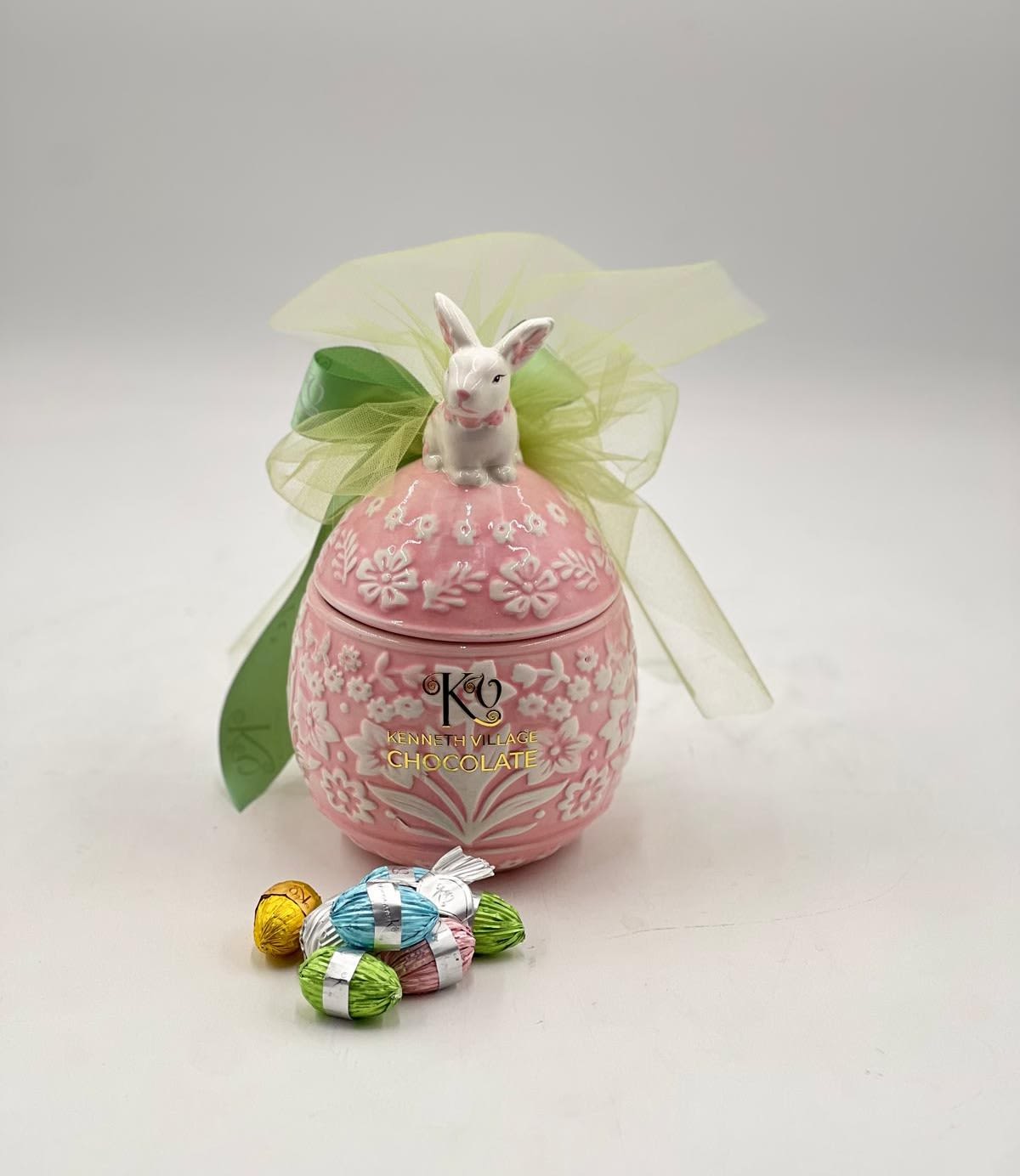 Easter Egg filled with Chocolates - A delicate and elegant Easter keepsake, this beautifully crafted pink ceramic egg container is adorned with embossed floral details and topped with a charming bunny figurine. Finished with a soft green ribbon, it opens to reveal a selection of premium wrapped chocolates in cheerful pastel hues. Both decorative and functional, this piece makes a timeless gift that captures the sweetness and beauty of the Easter season.