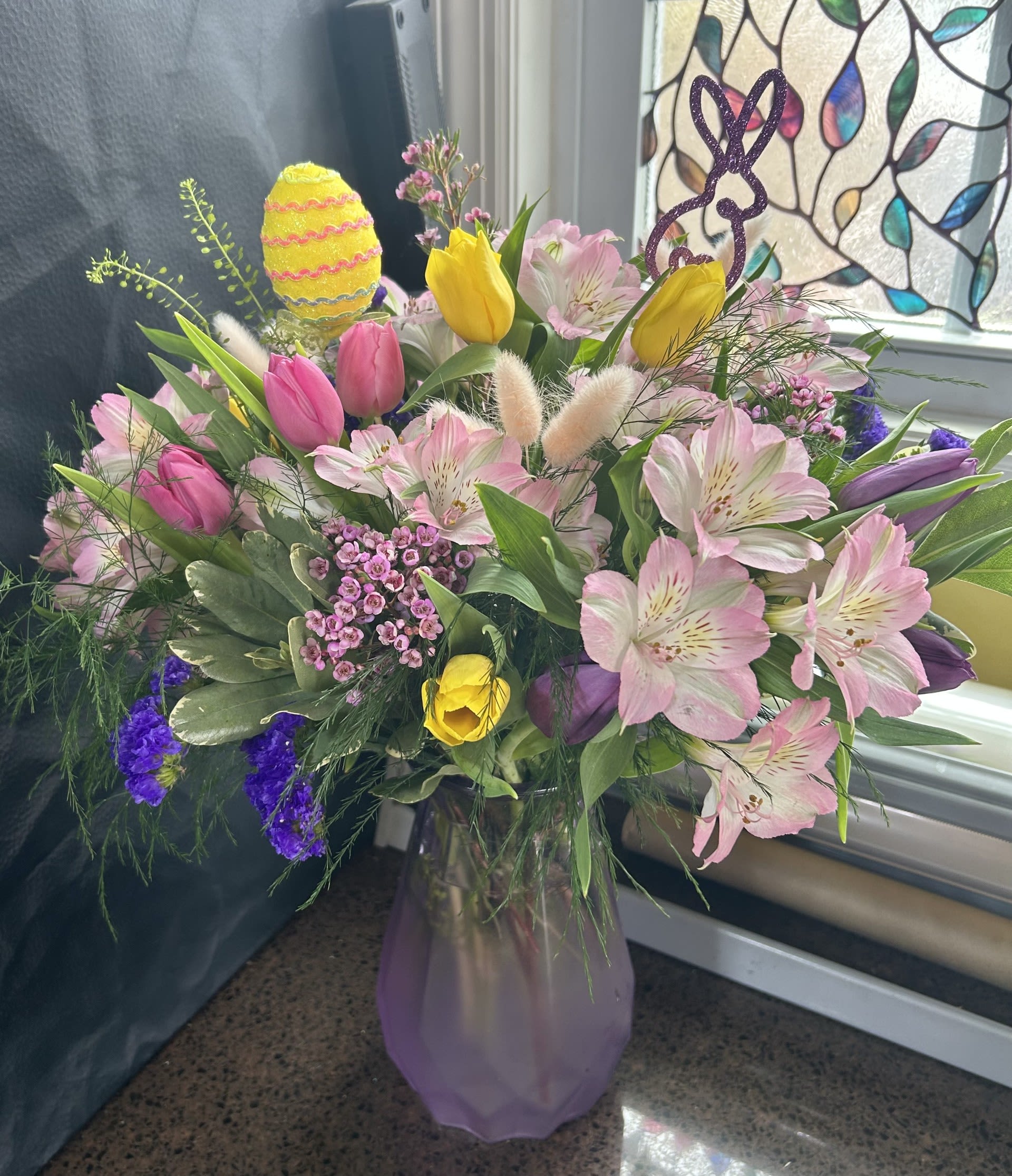 Happy Easter $75/100/125 - Lavendar keepsake vase 10" with soft pink Alstroemeria, colorful tulips, statice and wax flower dressed up for Easter celebration.