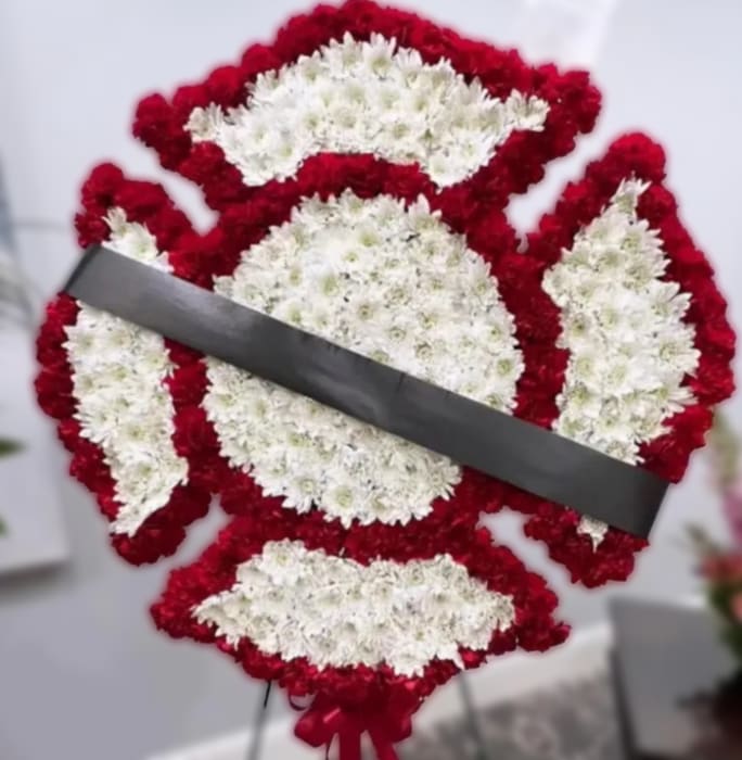 Fireman's Maltese Cross Tribute  - This specialty sympathy arrangement features a Fireman’s Maltese Cross design, created as a meaningful tribute to honor a life of service and dedication. Carefully crafted using fresh flowers, this piece offers a bold and respectful display suitable for funeral services or memorials. Designed approximately 24+ inches.  Due to the detailed design, this is a custom arrangement that requires additional time to create. Please allow adequate time before the service and call the shop to place your order.  If you would like a script included on the ribbon, please note your request in the florist note section when placing your order.  For delivery, please enter the name of the deceased in the recipient field and include the correct date of the service to ensure proper timing and placement. 