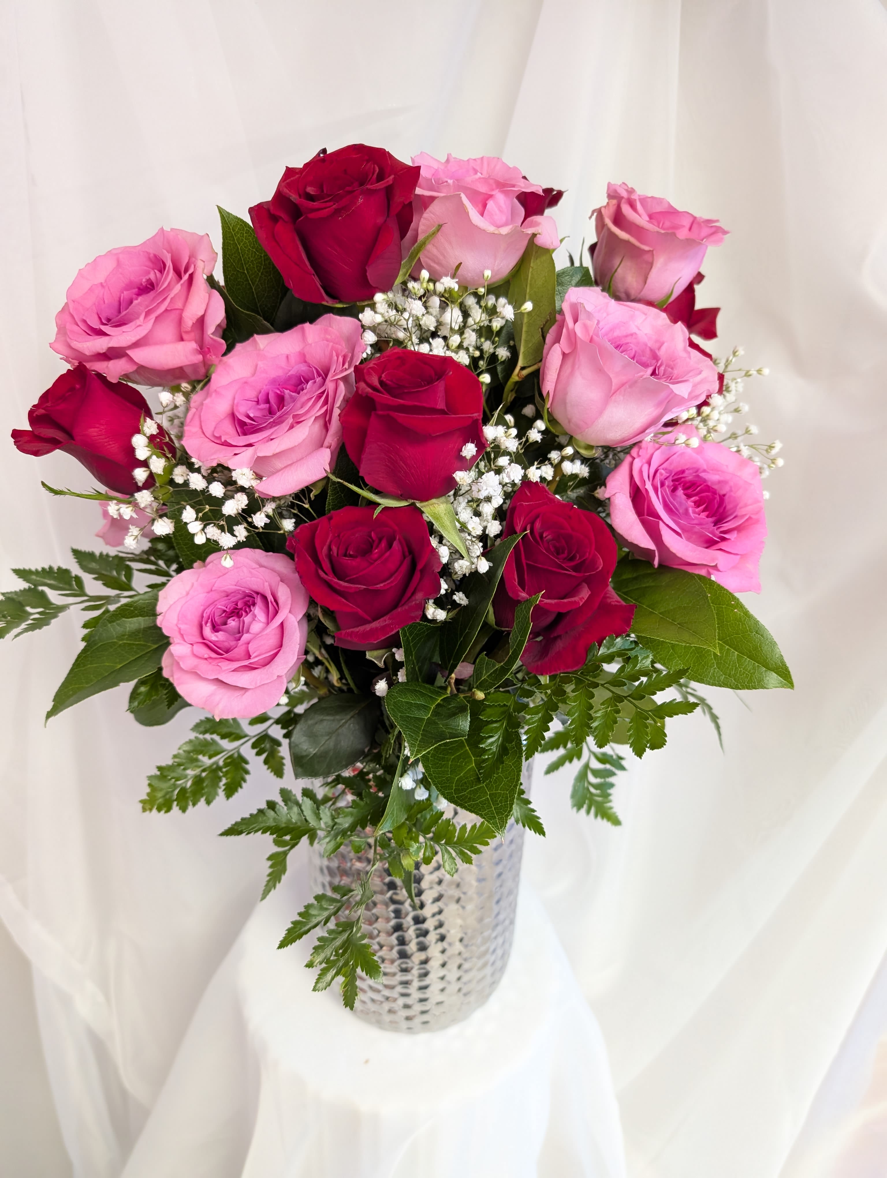 Tall arrangement of red and pink roses with baby's breath in a silver textured vase