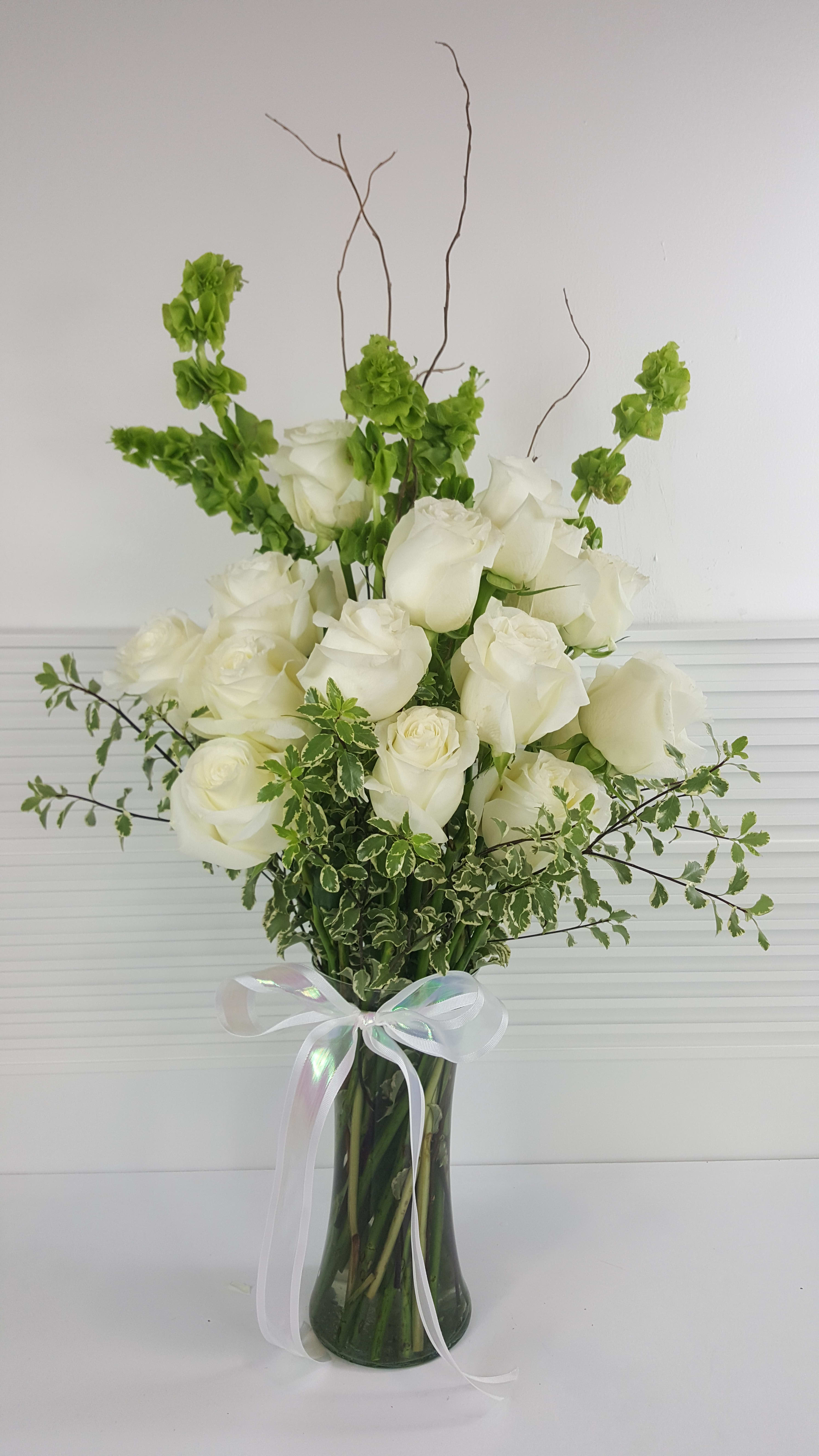 Tall arrangement of white roses and green Bells of Ireland in a clear vase with a white ribbon bow