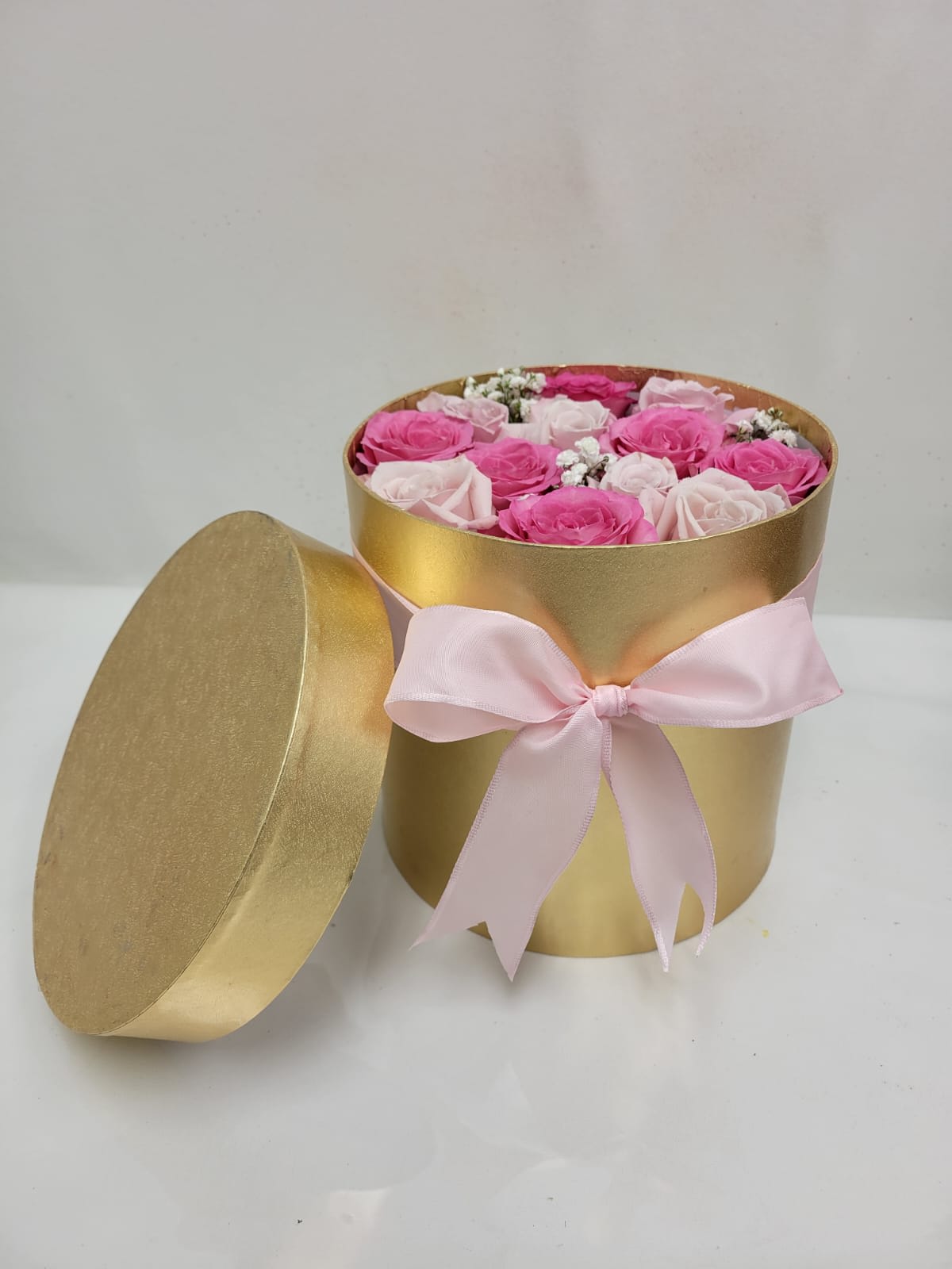 Round gold hatbox of pink and pale roses with lid and pink ribbon bow.