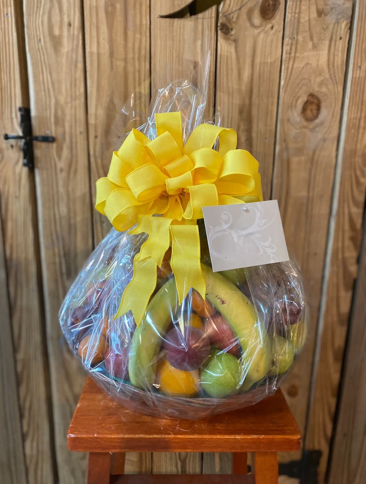 Wrapped fresh fruit basket with yellow bow and card on a wooden stool