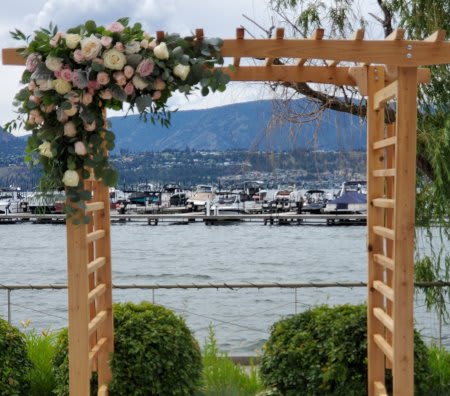 Wooden arbor with cascading blush and cream roses beside a lakeside marina.