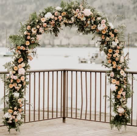 Large floral arch of peach and white blooms on a deck overlooking the water