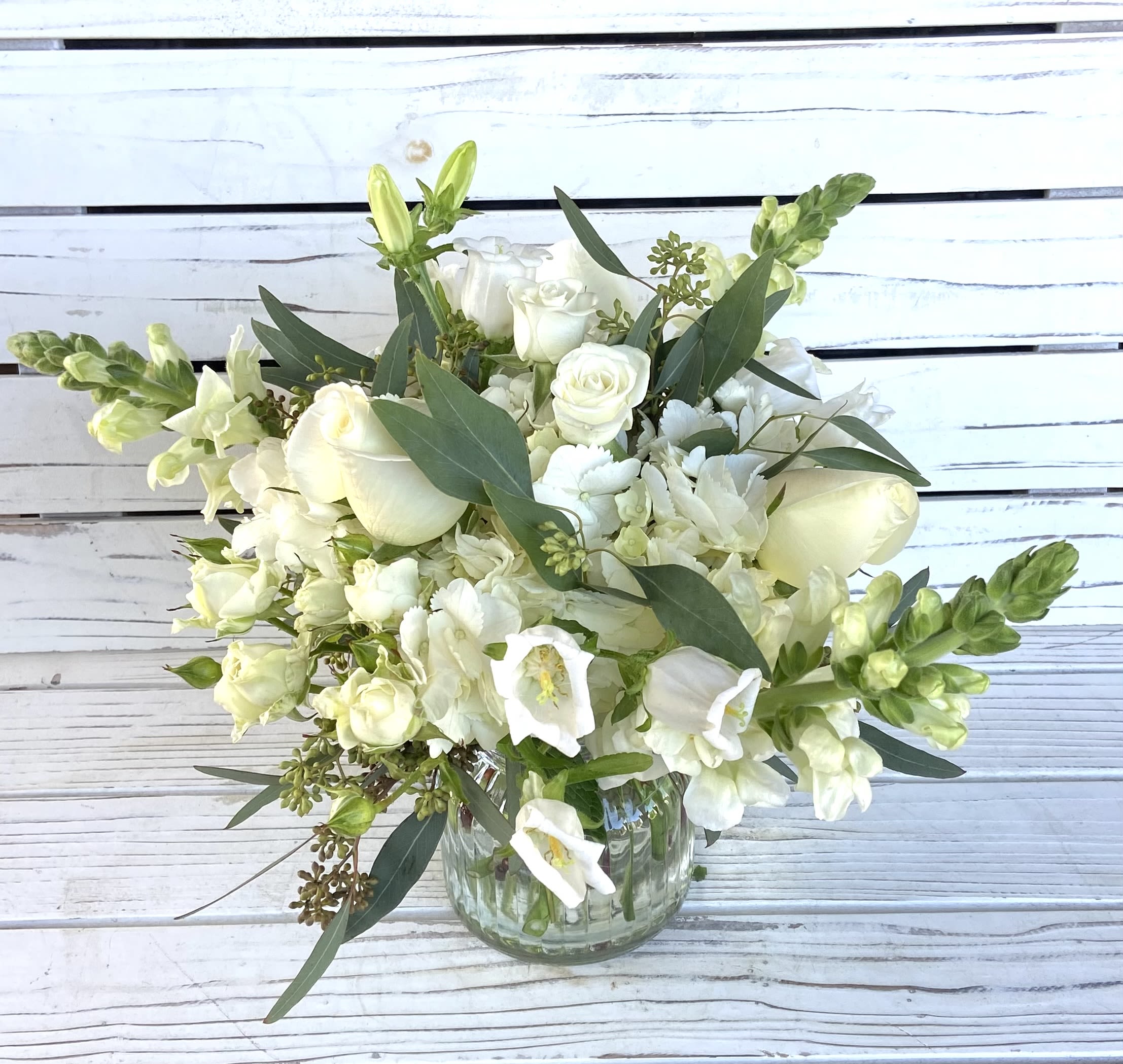 White flower arrangement with roses, hydrangea, and snapdragons in a clear glass vase