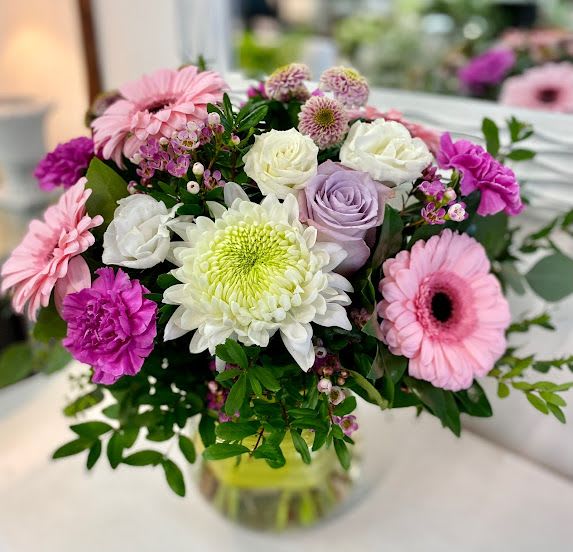 Mixed bouquet of pink gerbera daisies, roses, and a large white mum in a clear glass vase