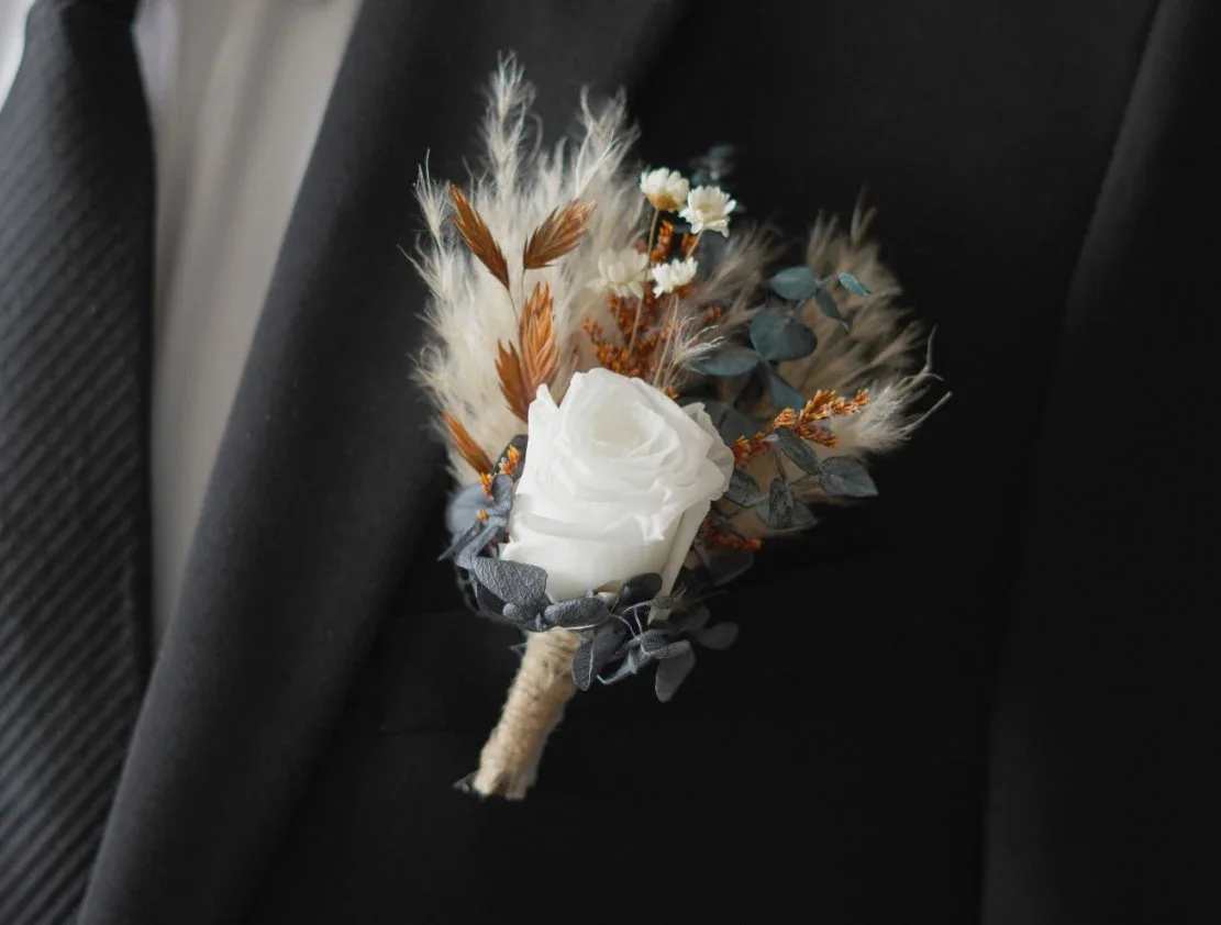 White rose boutonniere with dried accents on a black suit lapel