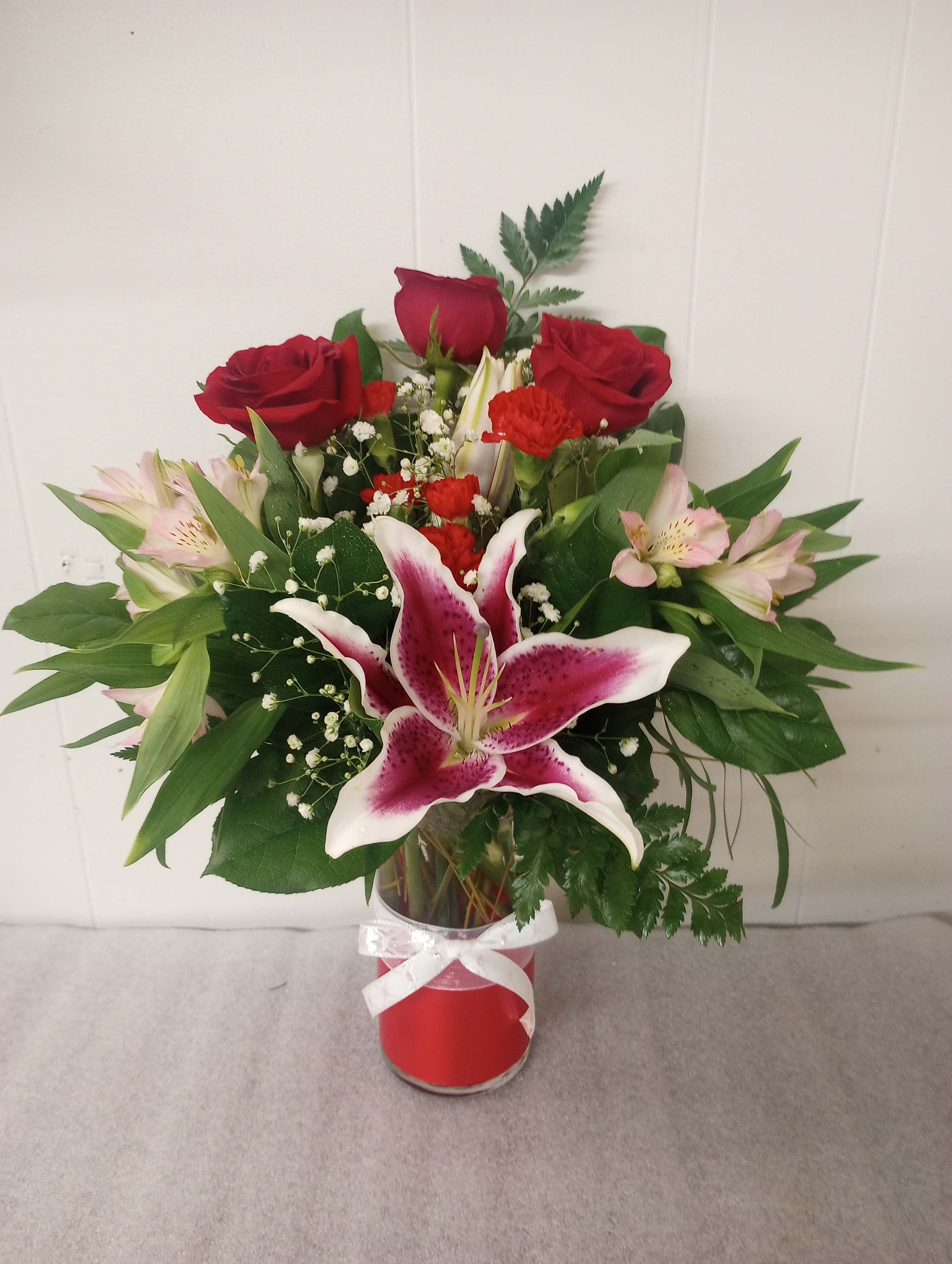 Red roses and pink lilies in a glass vase with a white ribbon