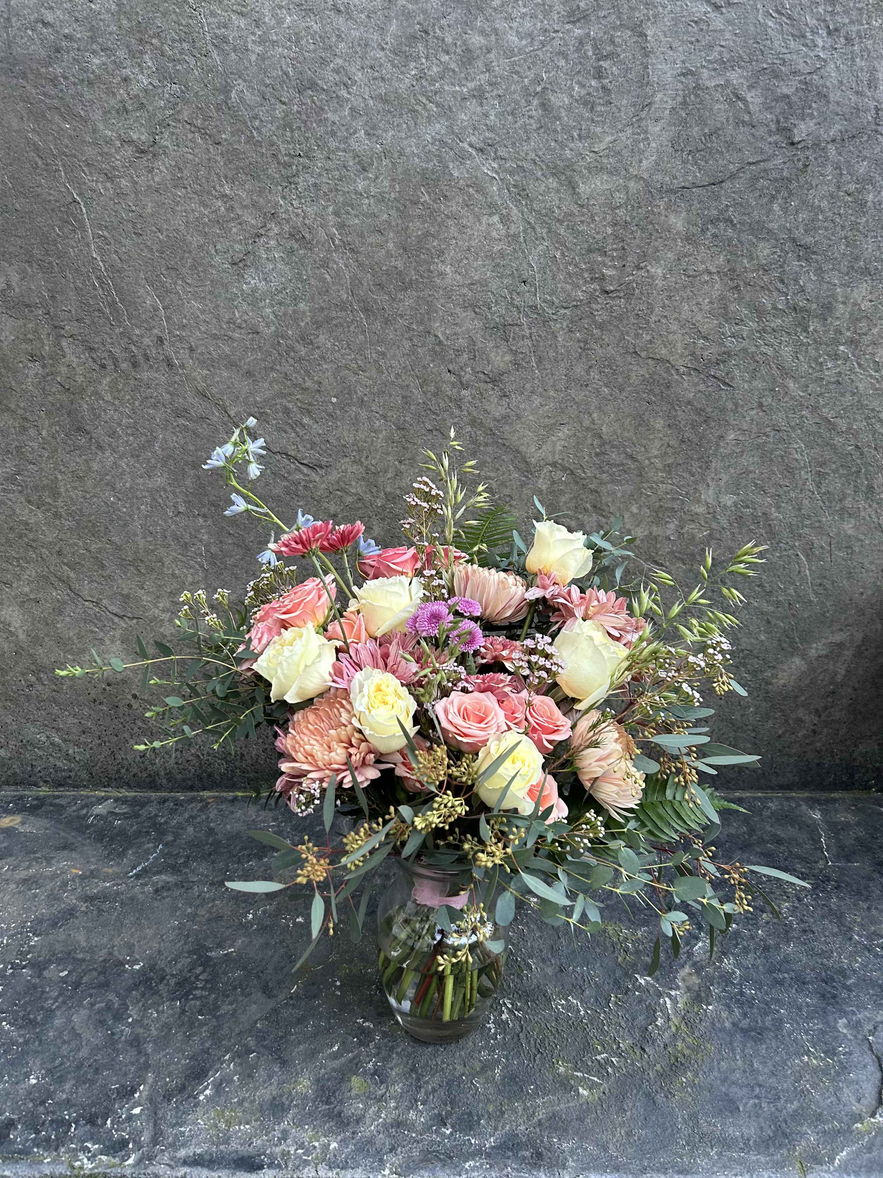 Raspberry Brulee - Cream roses, peach spray roses, blush and brown chrysanthemums with a touch of blue, grasses, ferns, eucalyptus and blooming fillers. in a glass vase or wrapped.   *reasonable substitutions may be made due to floral availability. Will have similar look and feel.
