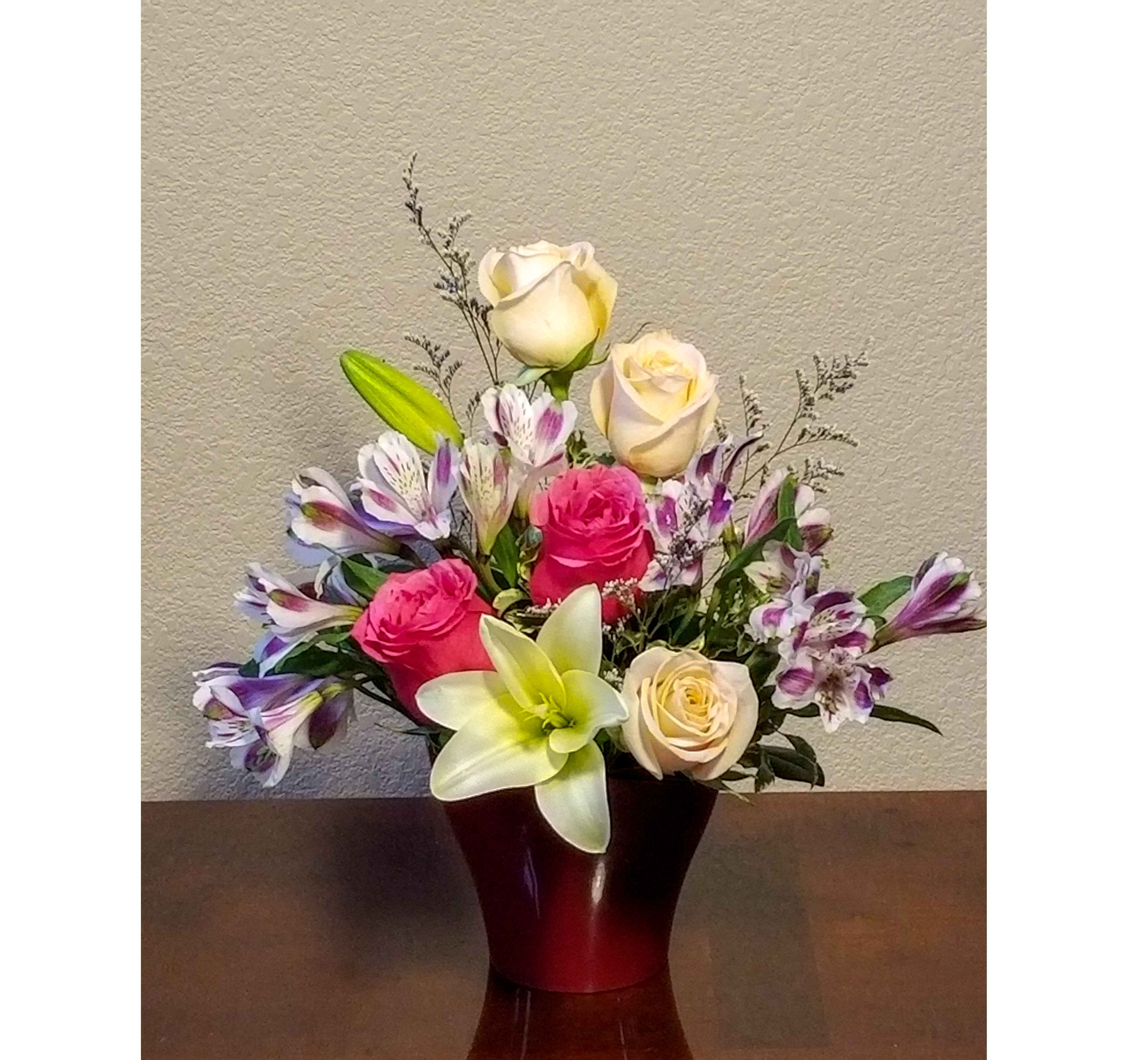 Mixed arrangement of pink and cream roses, lilies, and purple alstroemeria in a red vase