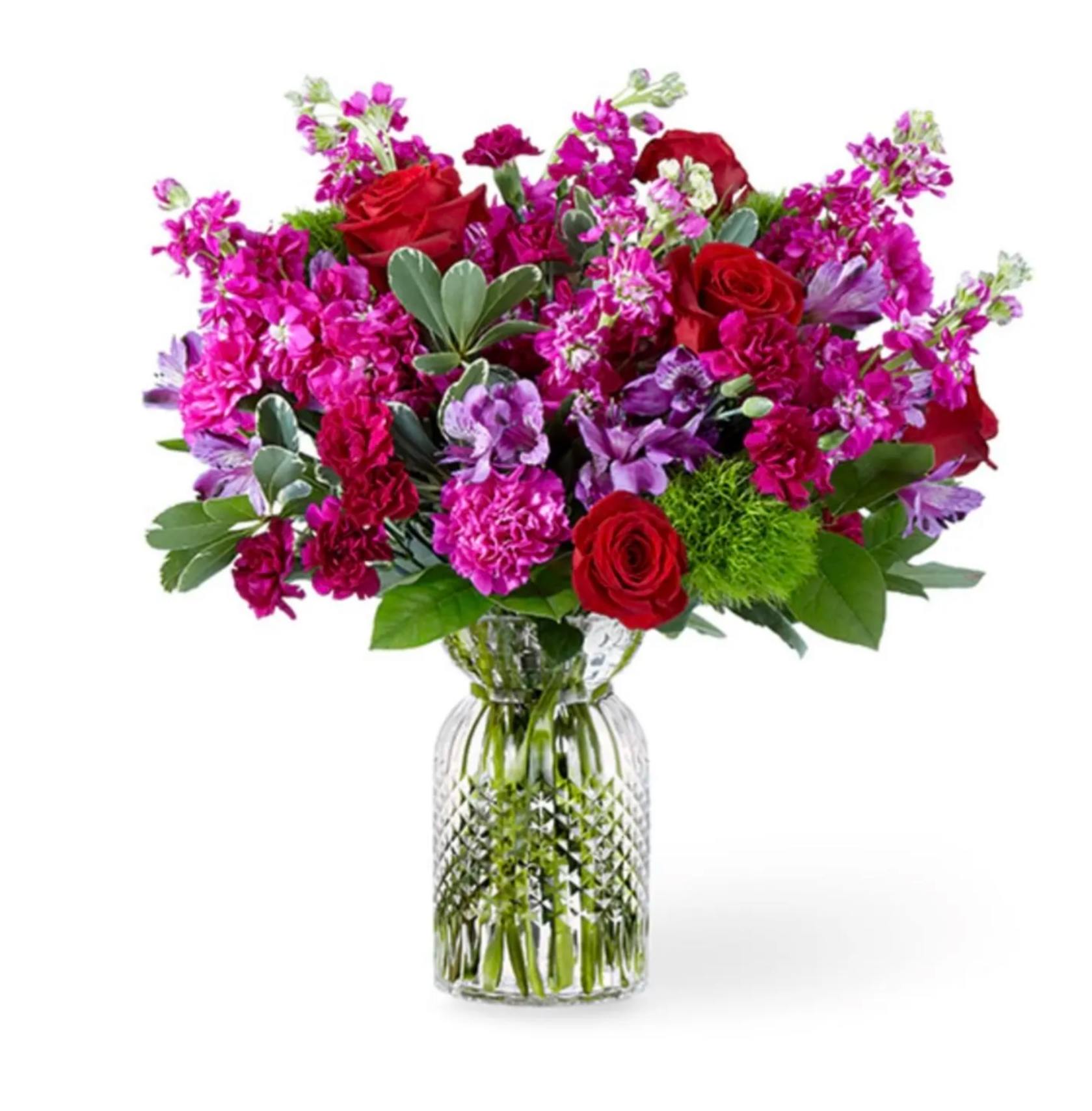 Jewel-tone bouquet of red roses, pink carnations, and purple blooms in a clear glass vase.