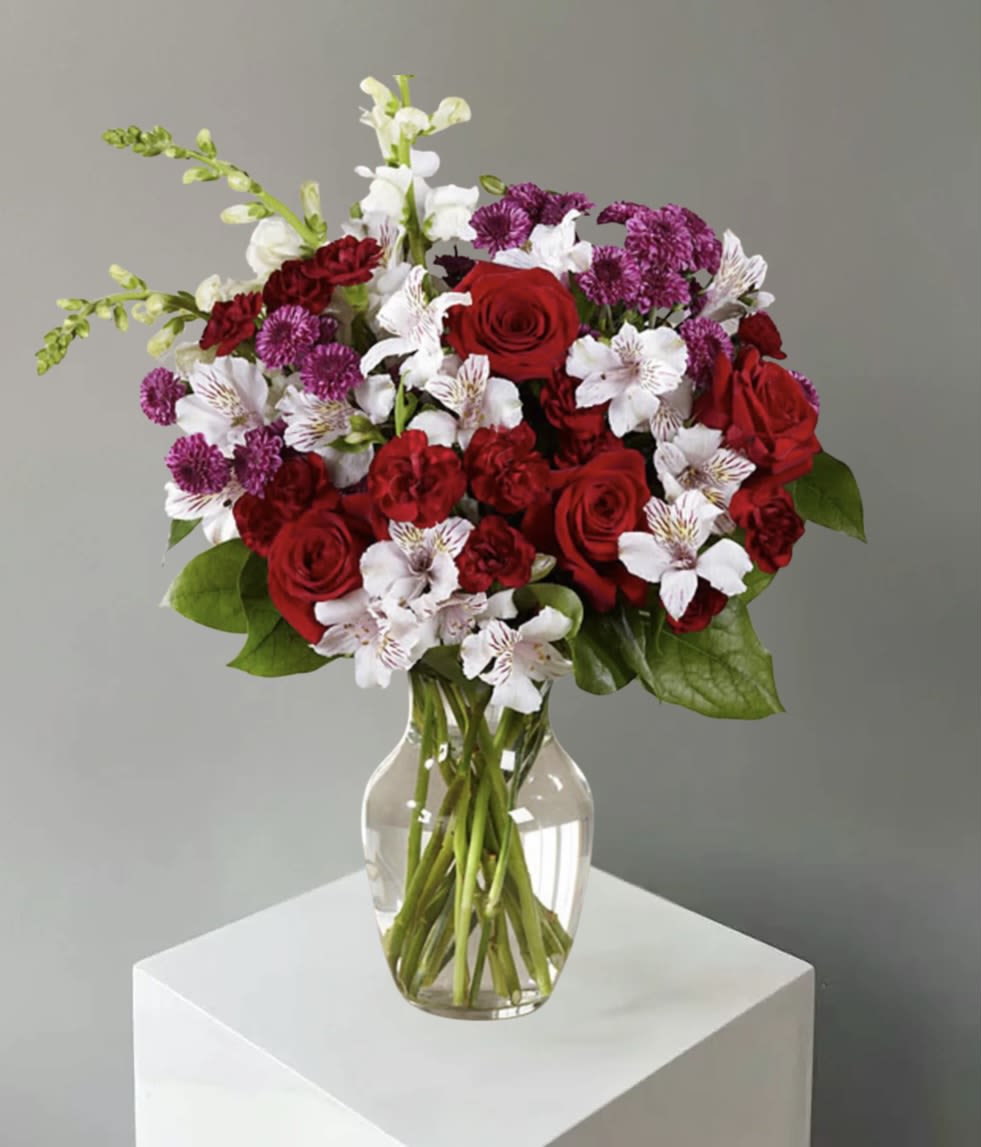 Bouquet of red roses, white alstroemeria, and purple carnations in a clear glass vase
