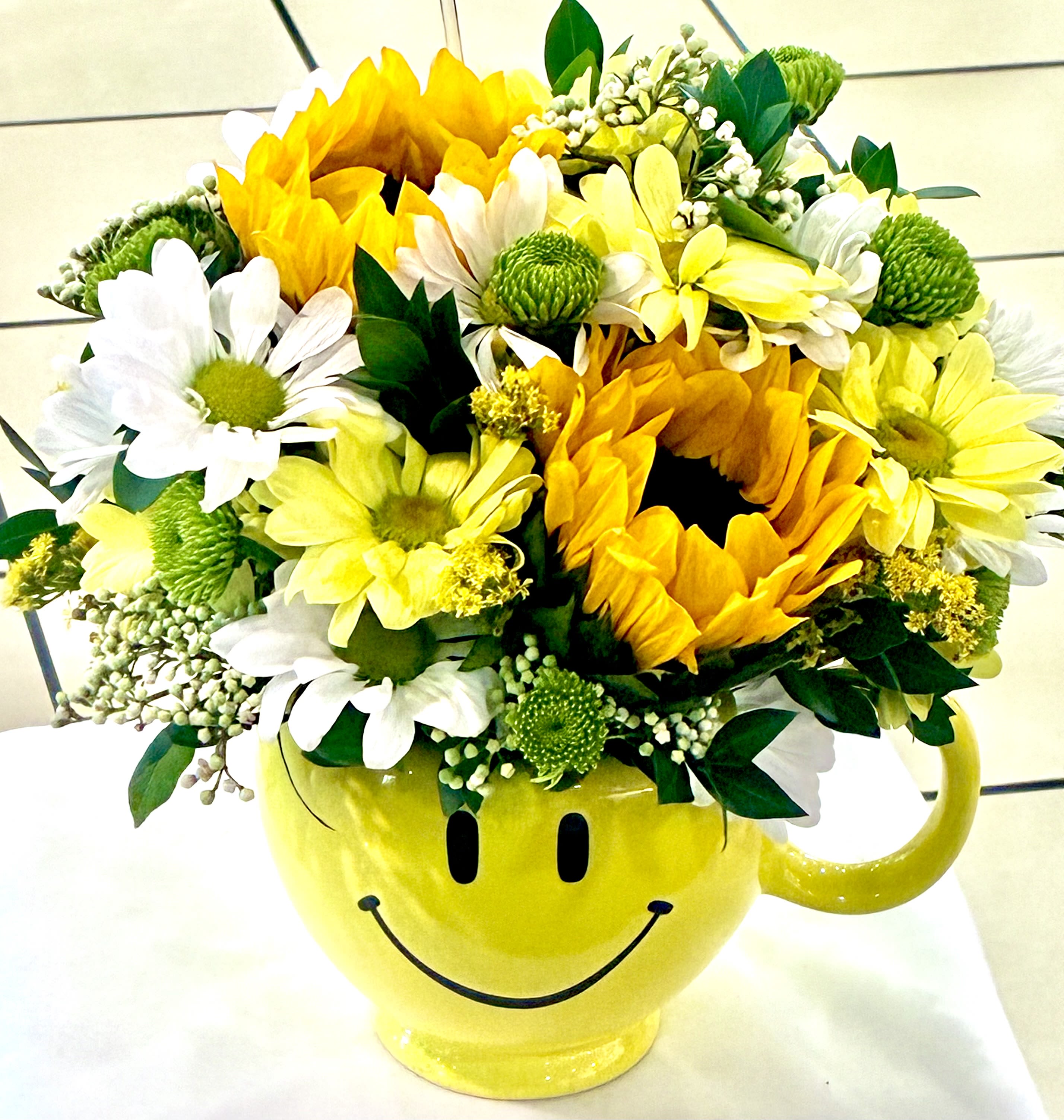 Smiley  - 2 Sun Flowers, 2 White Daisies, 2 Yellow Daisies, 2 Green Bottoms, White seeding eucalyptus, greens, yellow smiley vase.  1/2 blocks of floral foam  " Standard" 2 Yellow Rose, 2 Sun Flowers, 2 White Daisies, 2 Yellow Daisies, 2 Green Bottoms, White seeding eucalyptus, greens, yellow smiley vase.  1/2 blocks of floral foam  "Deluxe"  4 Yellow rose, 2 Sun Flowers, 2 White Daisies, 2 Yellow Daisies, 2 Green Bottoms, White seeding eucalyptus, greens, yellow smiley vase.  1/2 blocks of floral foam  "Premium"