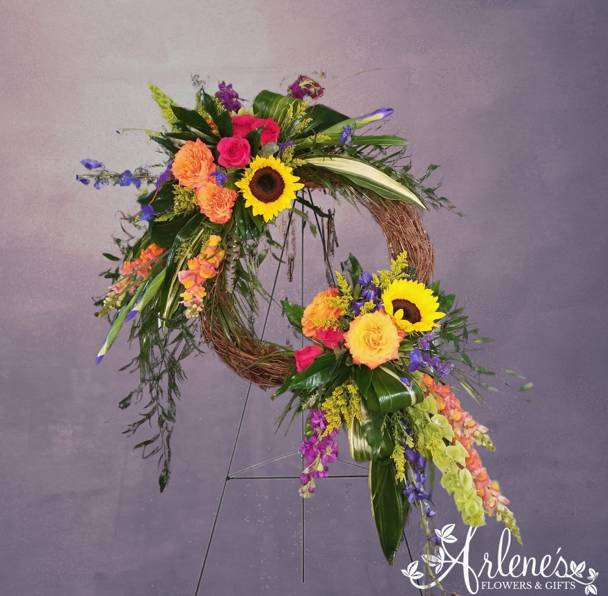 Garden Grapevine Wreath - A gathering of beautiful flowers artfully grace a grapevine wreath. Shown here is a wildflower color mix. The designer will choose the best flowers of quality to do a similar design.