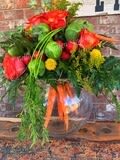 Arrangement of mixed red and green blooms with carrots in a round glass bowl vase