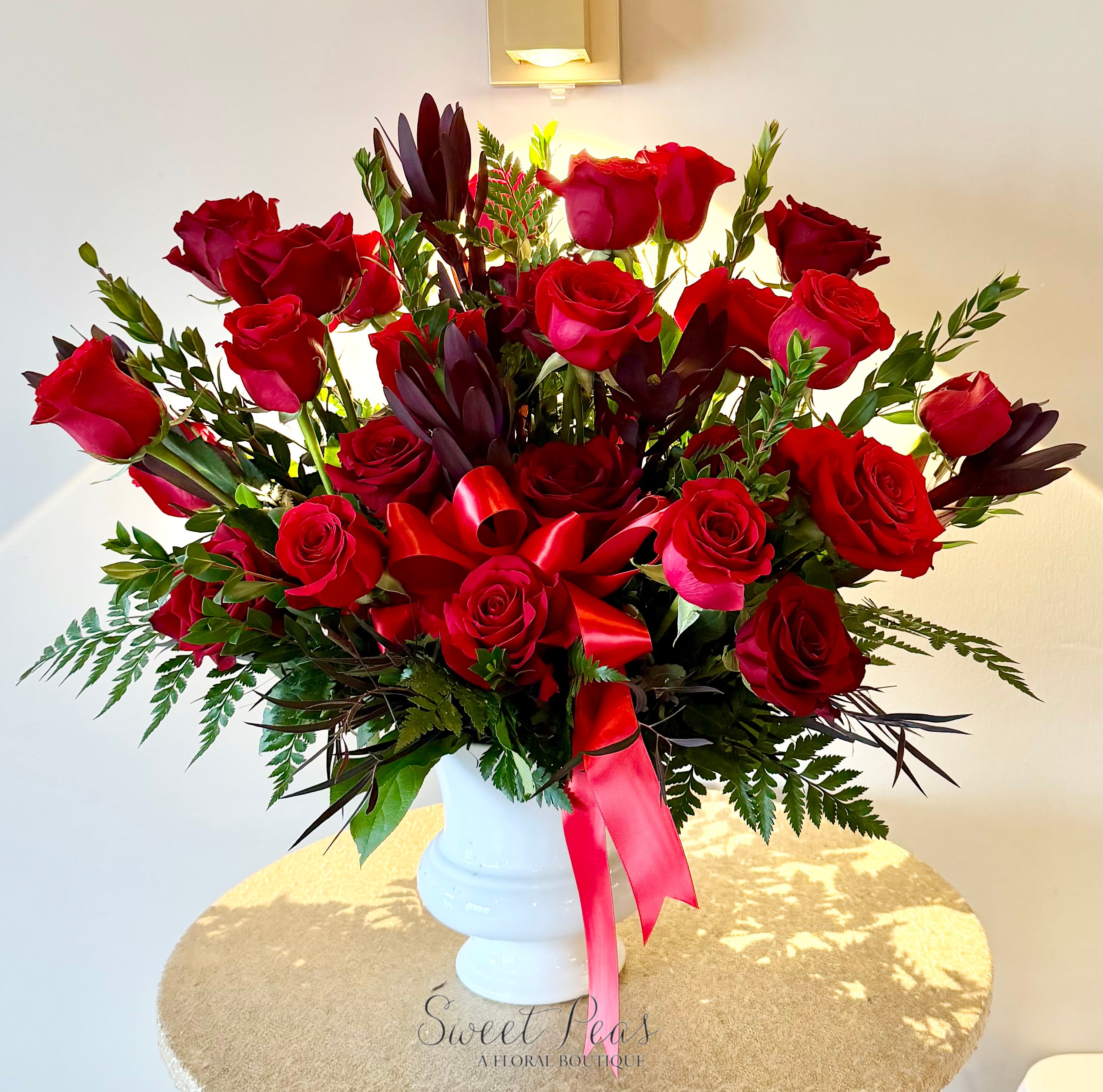 Forever In Our Hearts - Elegant and deeply meaningful, Forever in Our Hearts features a lush gathering of premium red roses accented with rich greenery and finished with a classic satin ribbon. Symbolizing love, respect, and remembrance, this timeless arrangement offers a heartfelt expression of sympathy and support. Designed in a classic white vessel, it serves as a beautiful tribute to honor a life well lived and a love that endures.