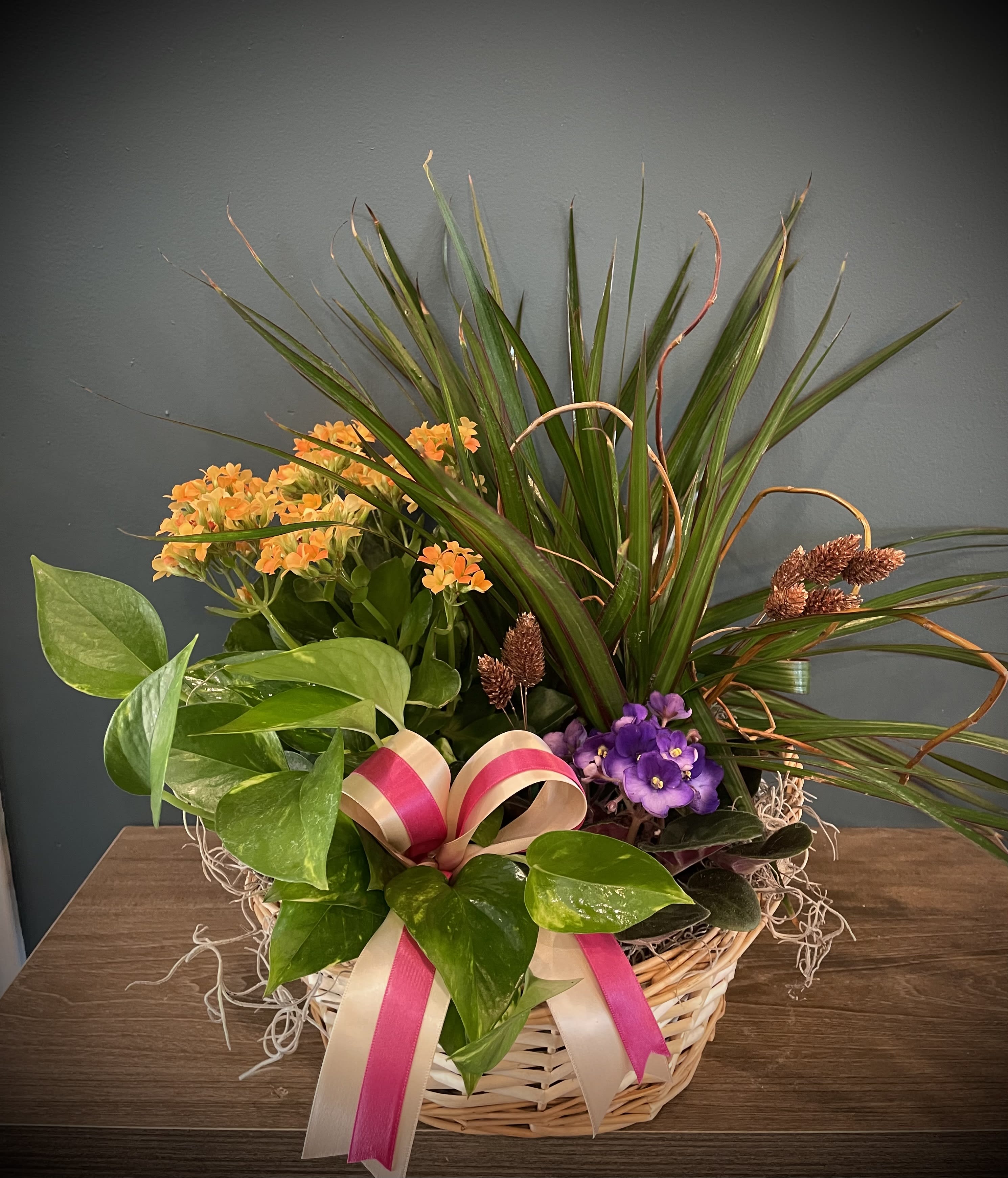 Basket arrangement with orange and purple flowers and a pink ribbon