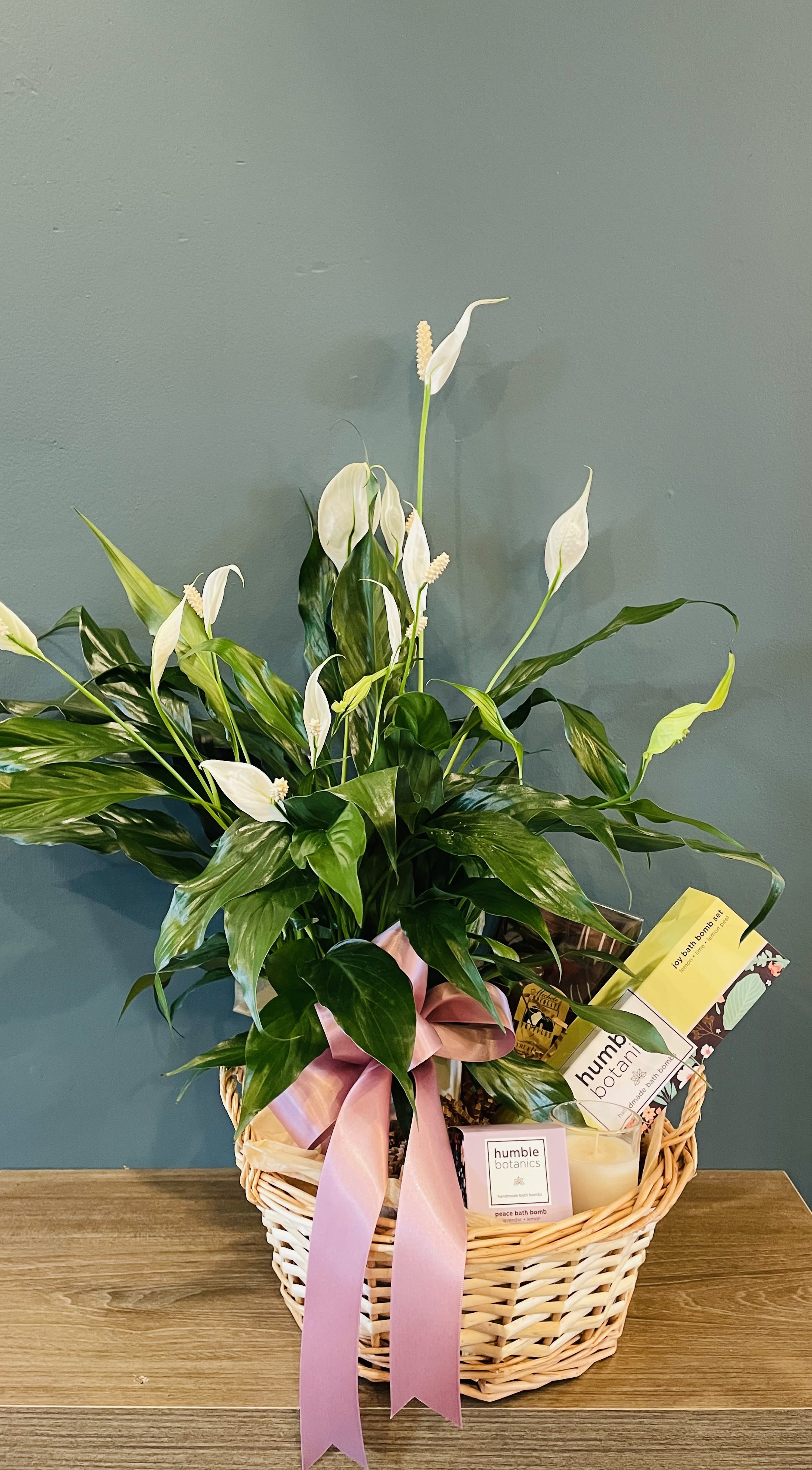 Basket gift with white peace lilies and bath products tied with a pink ribbon