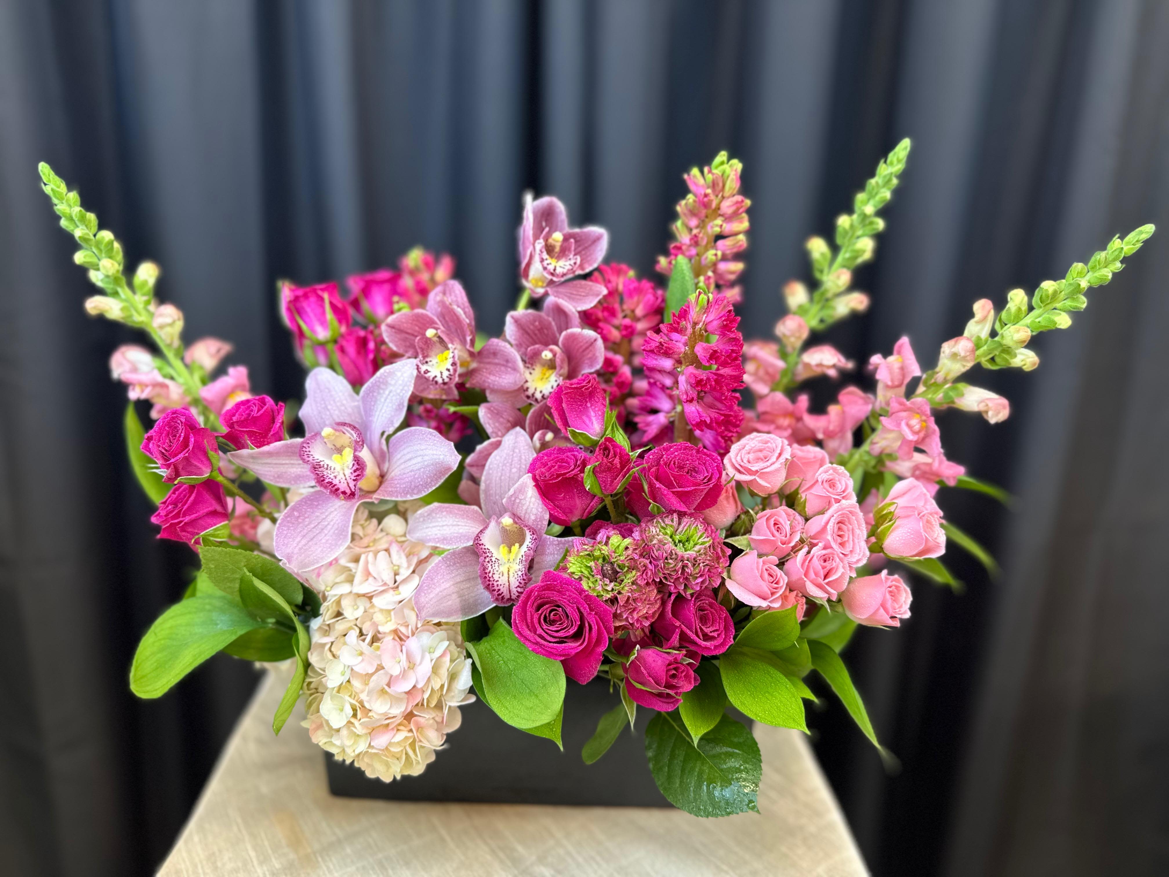 Pink Obsession  - Pink Obsession is a striking, high-end arrangement that celebrates the beauty of pink in every shade. Featuring elegant orchids, lush roses, delicate snapdragons, and full hydrangea, this design is layered with texture and depth. Arranged in a sleek black rectangular container, the soft blush and vibrant pink tones create a bold, modern contrast—perfectly balancing romance with sophistication.