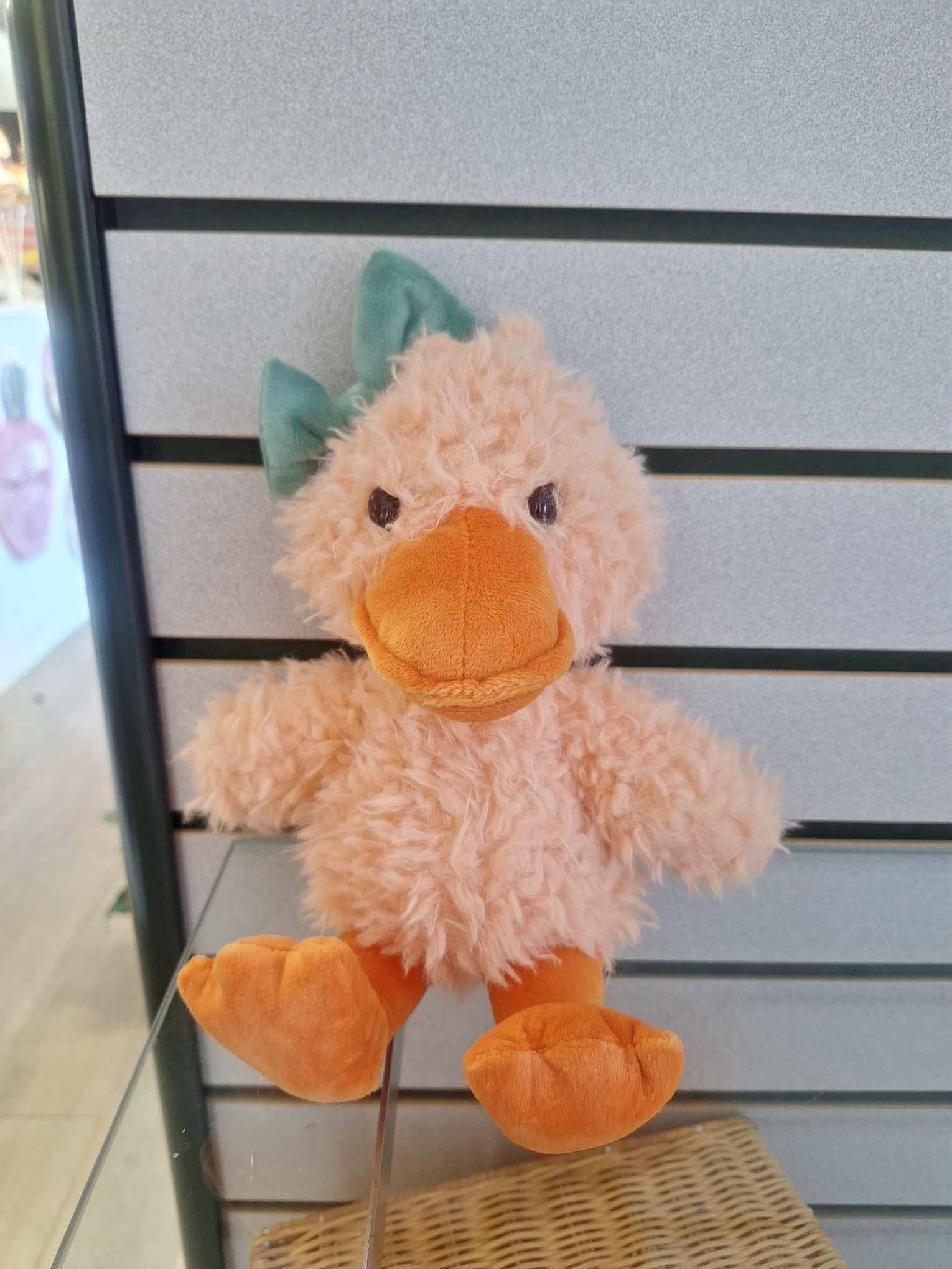 Small plush duck toy with fuzzy peach body, orange beak and feet, and a green bow.