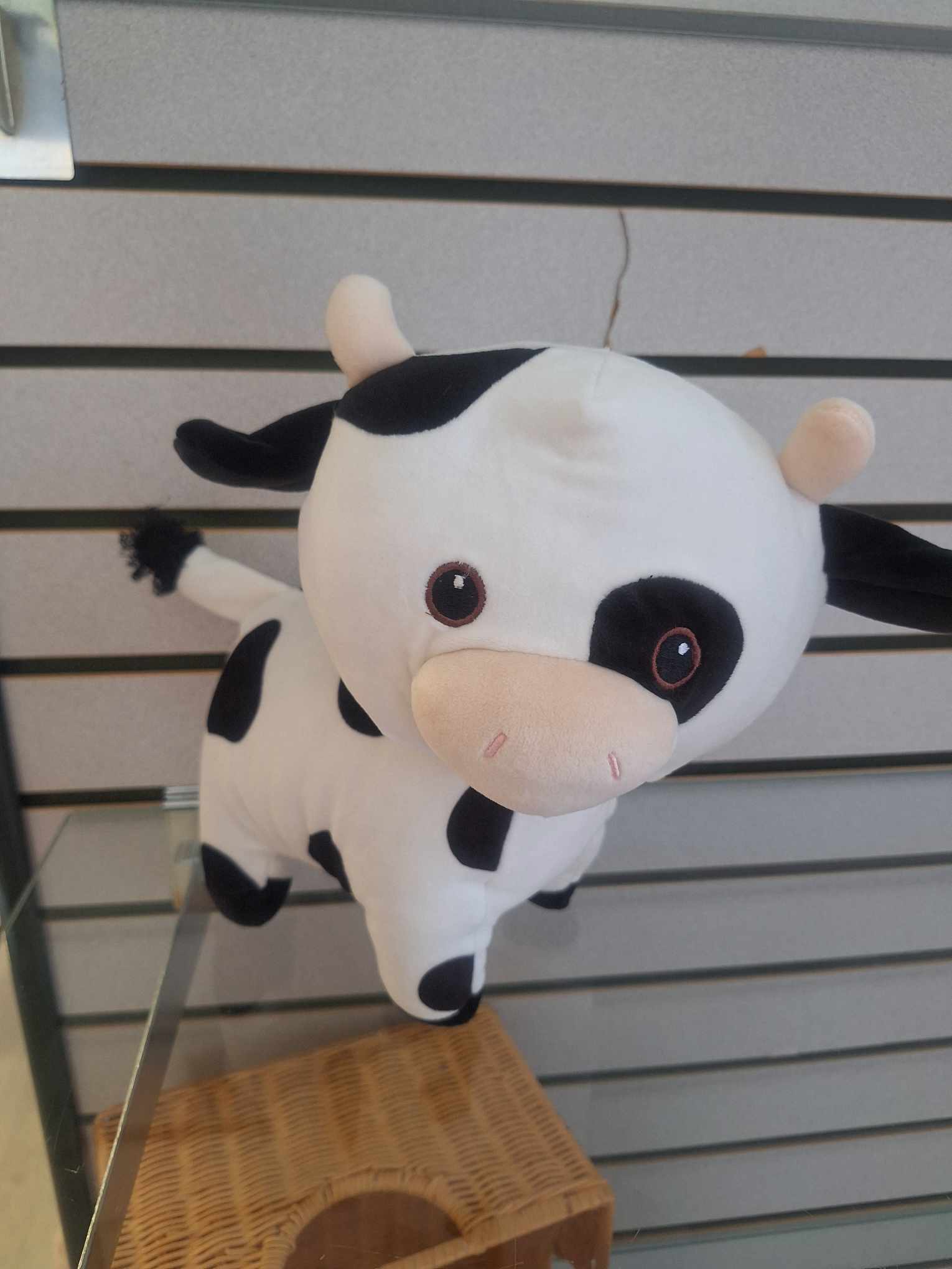Small black and white cow plush toy with pink snout on a display shelf.
