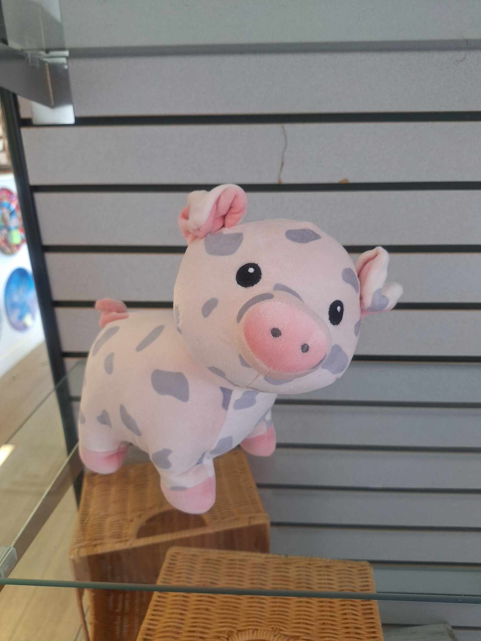 Small pink plush pig with gray spots displayed on a glass shelf.