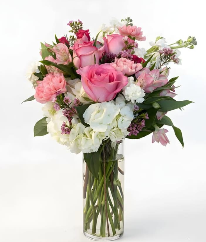 Blushing Garden Bouquet - A soft, romantic mix of pink roses, blush carnations, delicate alstroemeria, and white hydrangea, accented with airy filler and fresh greenery. Designed in a clear glass vase, this arrangement feels light, feminine, and perfect for spring celebrations, birthdays, or just because.