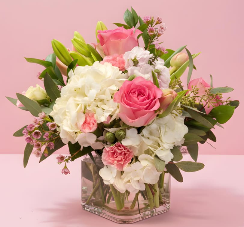 Sweet Blush Cube - A soft and elegant arrangement featuring lush white hydrangea, premium pink roses, delicate spray roses, and blush carnations, accented with fresh greenery and seasonal blooms. Designed in a modern glass cube vase, this piece offers a clean, romantic look that’s perfect for everyday moments, sympathy gestures, or sweet celebrations.