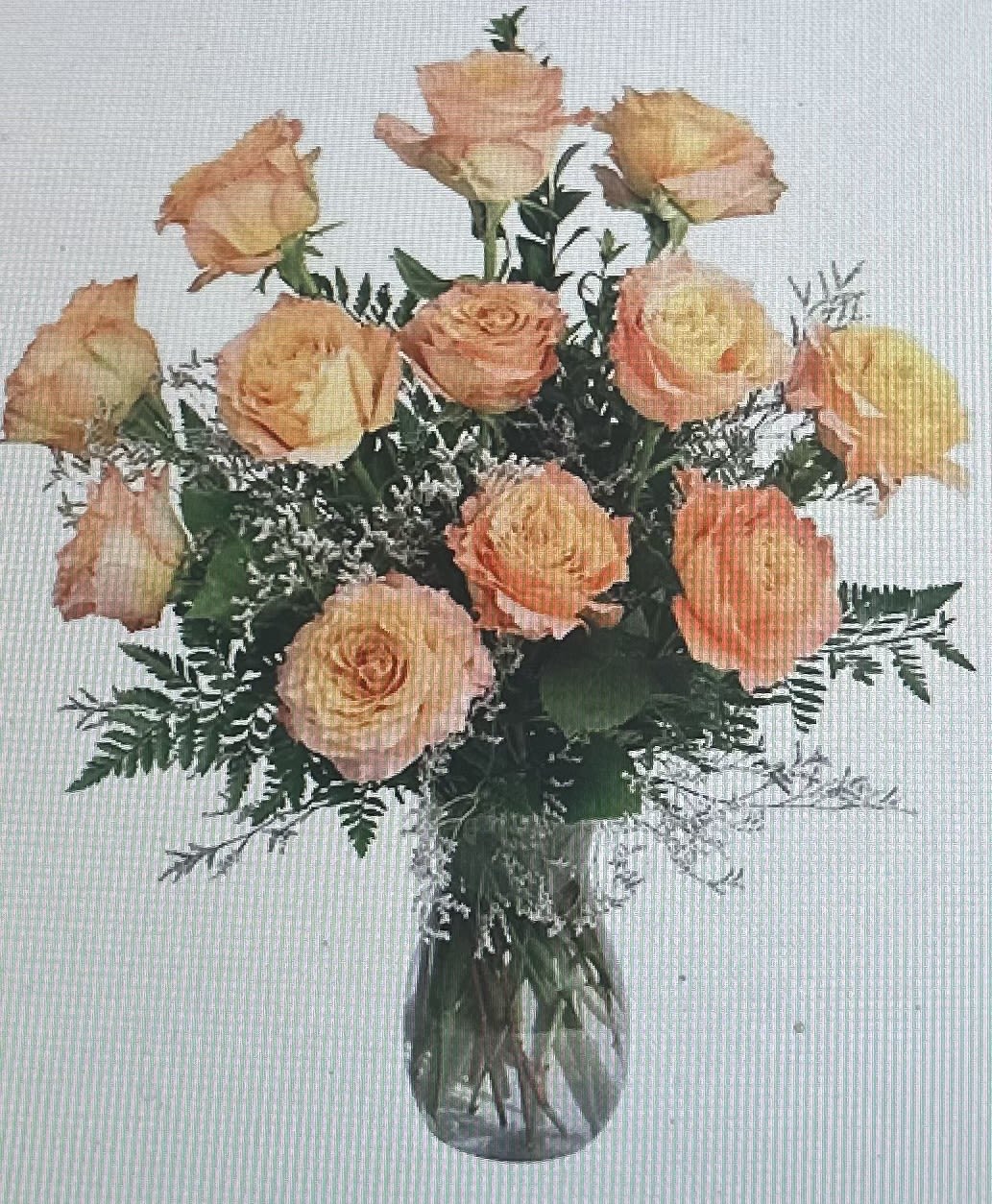 Arrangement of peach roses with white filler flowers in a clear glass vase