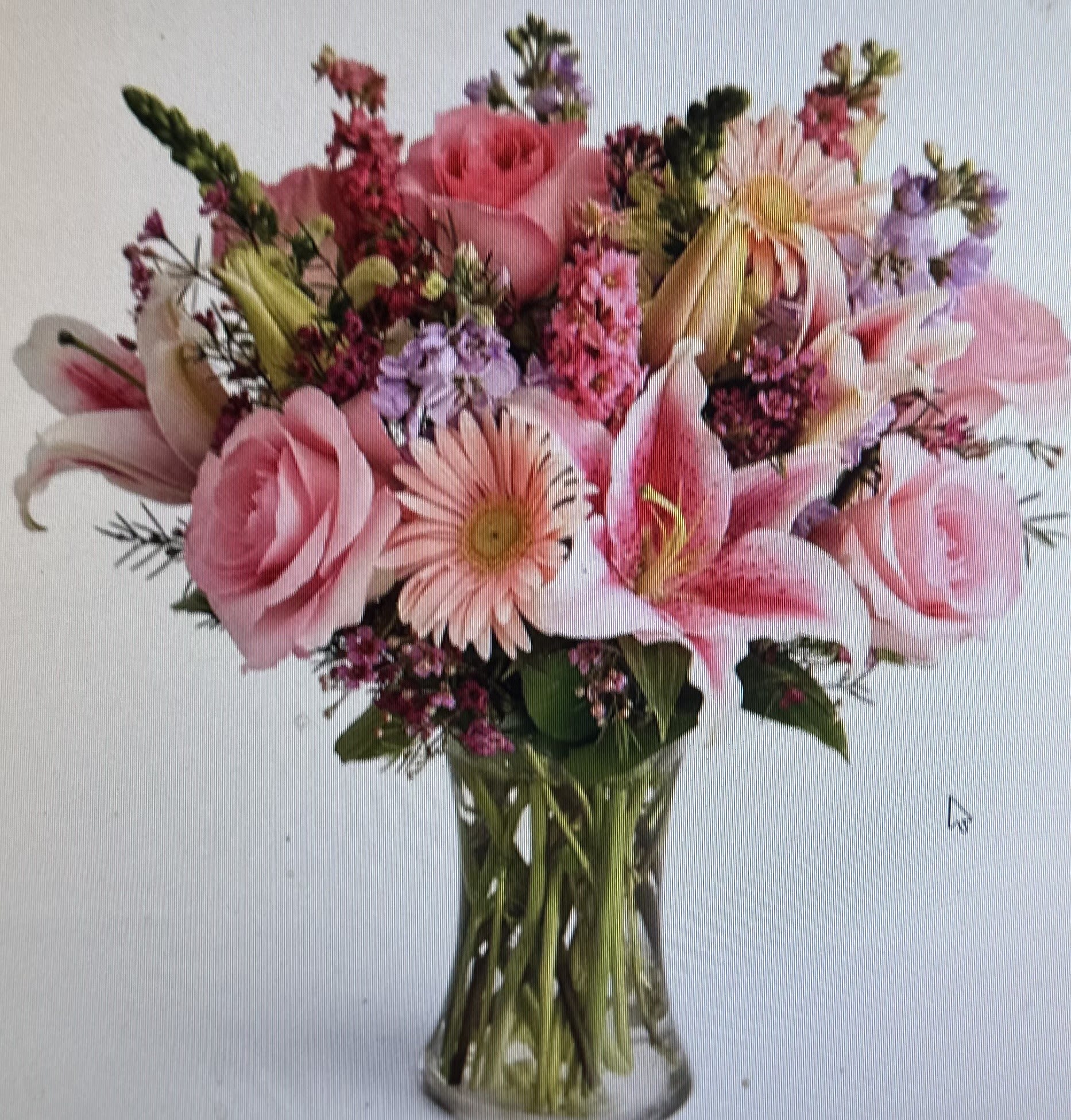 Pink roses, lilies, and gerbera daisies arranged in a clear glass vase