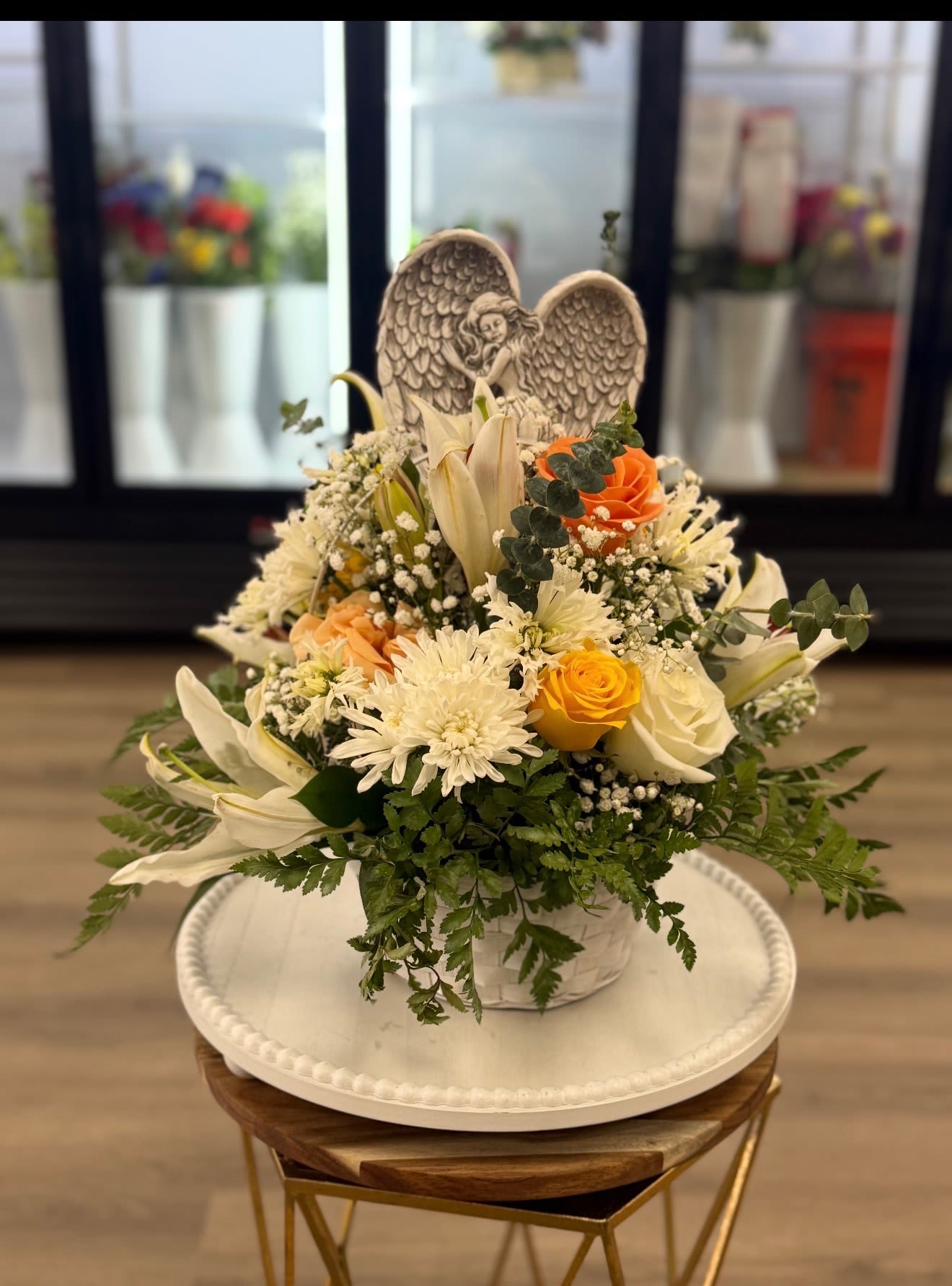 White and peach floral basket with roses, lilies, and an angel figurine.