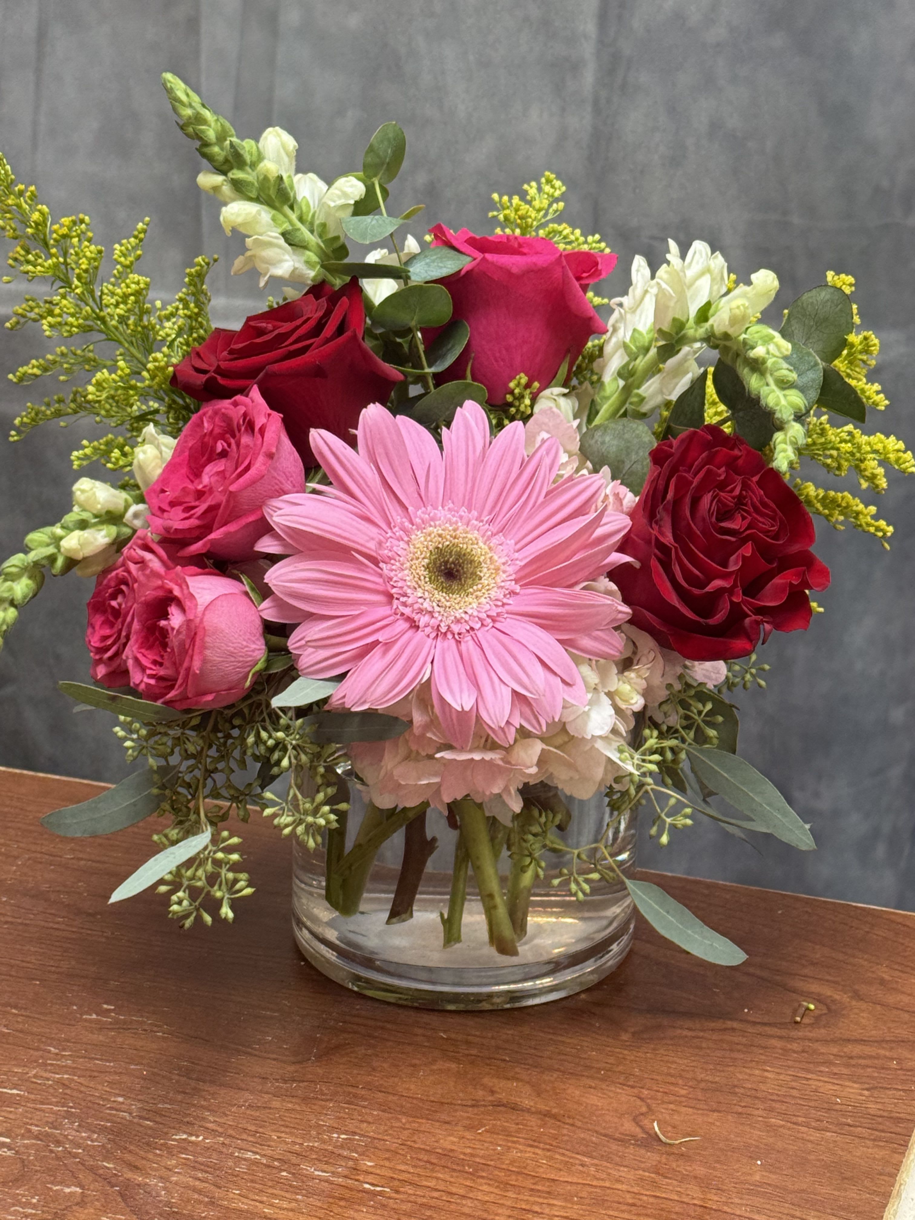 Love in Bloom Vase - A beautiful mix of red roses, pink gerbera, and seasonal blooms arranged in a clear glass vase. A perfect gift to express love, joy, and appreciation for any occasion.