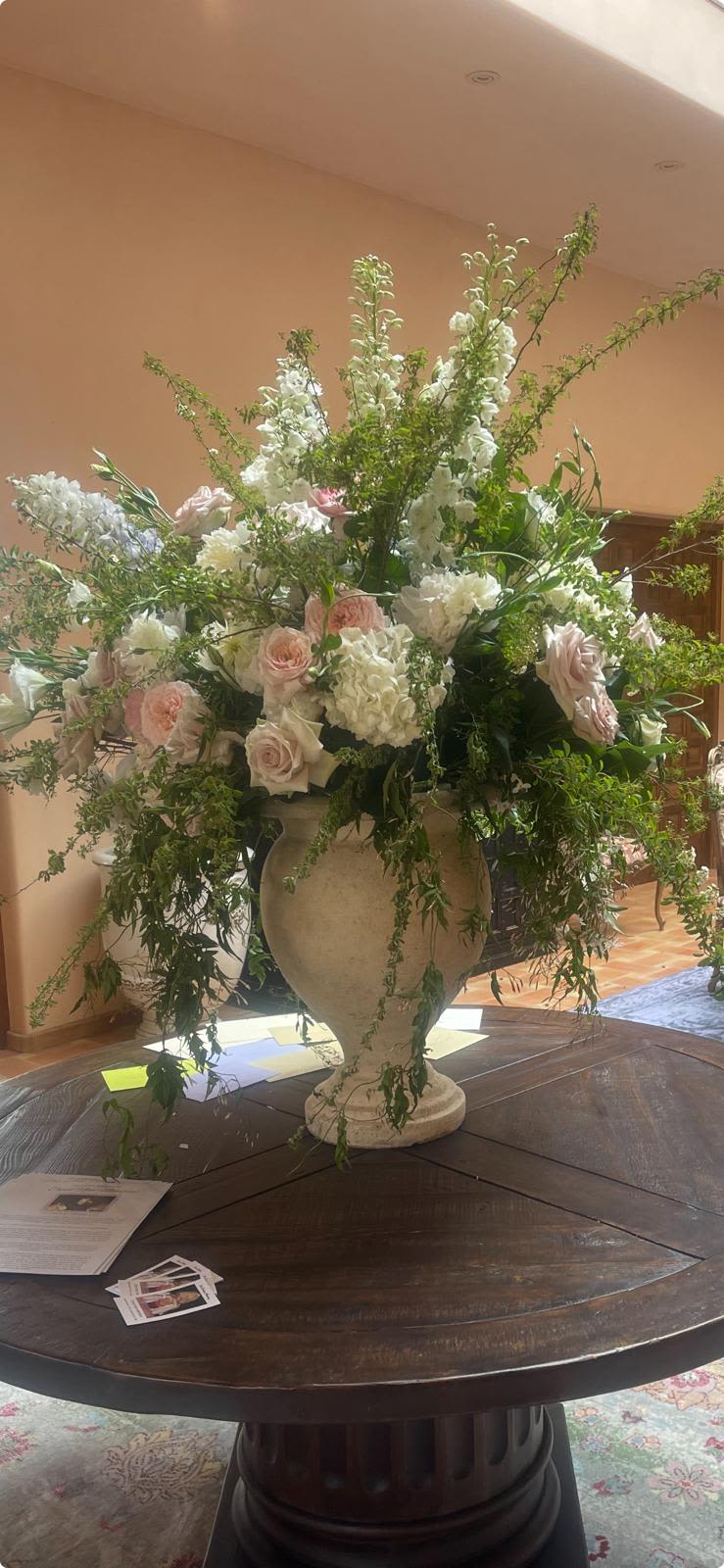Large urn arrangement with white and blush flowers and cascading greenery on a round wooden table