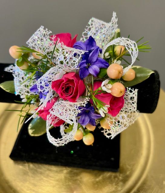 Sabrina - Wristlet on a classic band filled with bright pink spray roses, peach berries, purple hyacinth and a white ribbon that sparkles. 