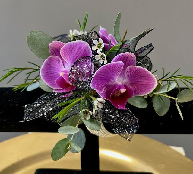 Billie  - Stunning purple orchids tucked into black ribbon accented with white wax flower and eucalyptus. This comes on a standard wristlet band that is silver.